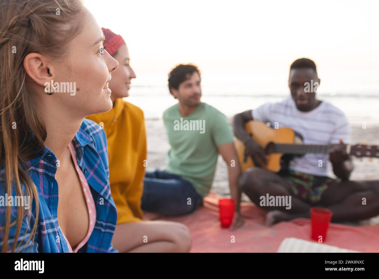 Amici diversi si godono una riunione sulla spiaggia al tramonto, con una festa Foto Stock