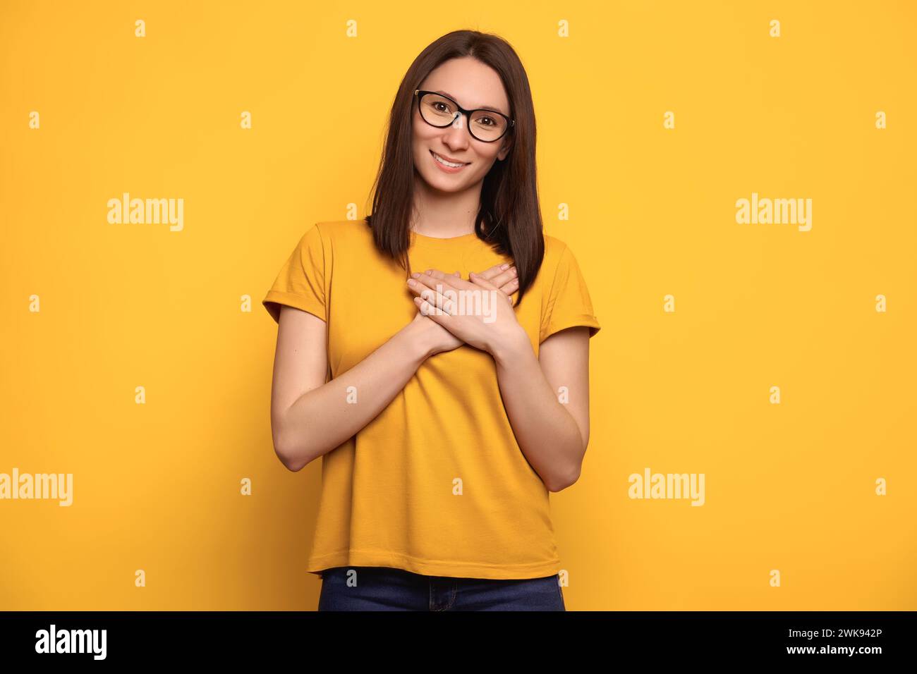 Felice e pacifico donna millenaria in abiti casual su sfondo giallo studio tenendosi per mano al petto vicino al cuore, sorridente grata, si sente grata, mostra apprezzamento. Credere e amare il concetto Foto Stock