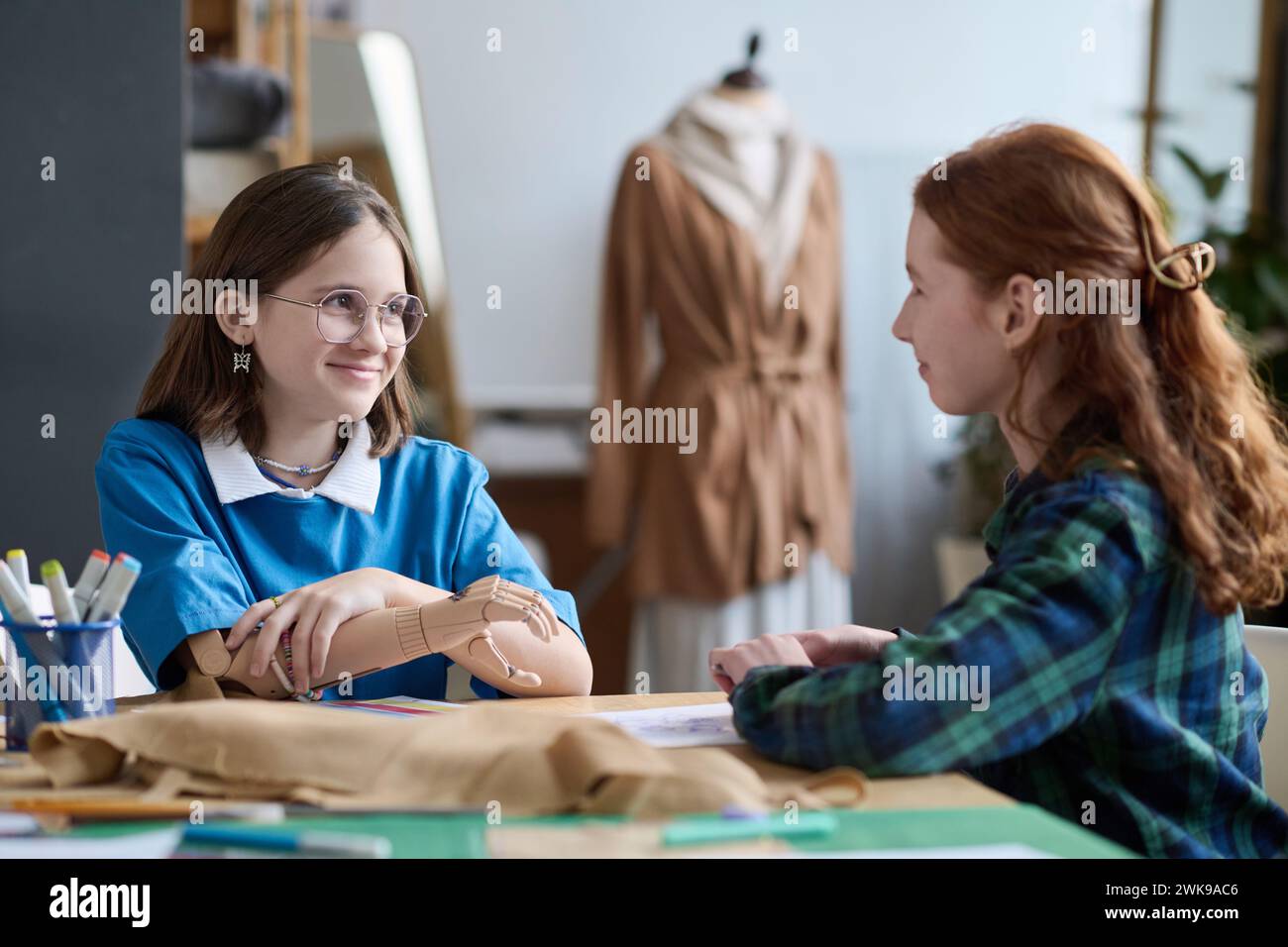 Ritratto di una giovane ragazza sorridente con una protesi che chiacchiera con un amico durante la lezione di sartoria a scuola Foto Stock