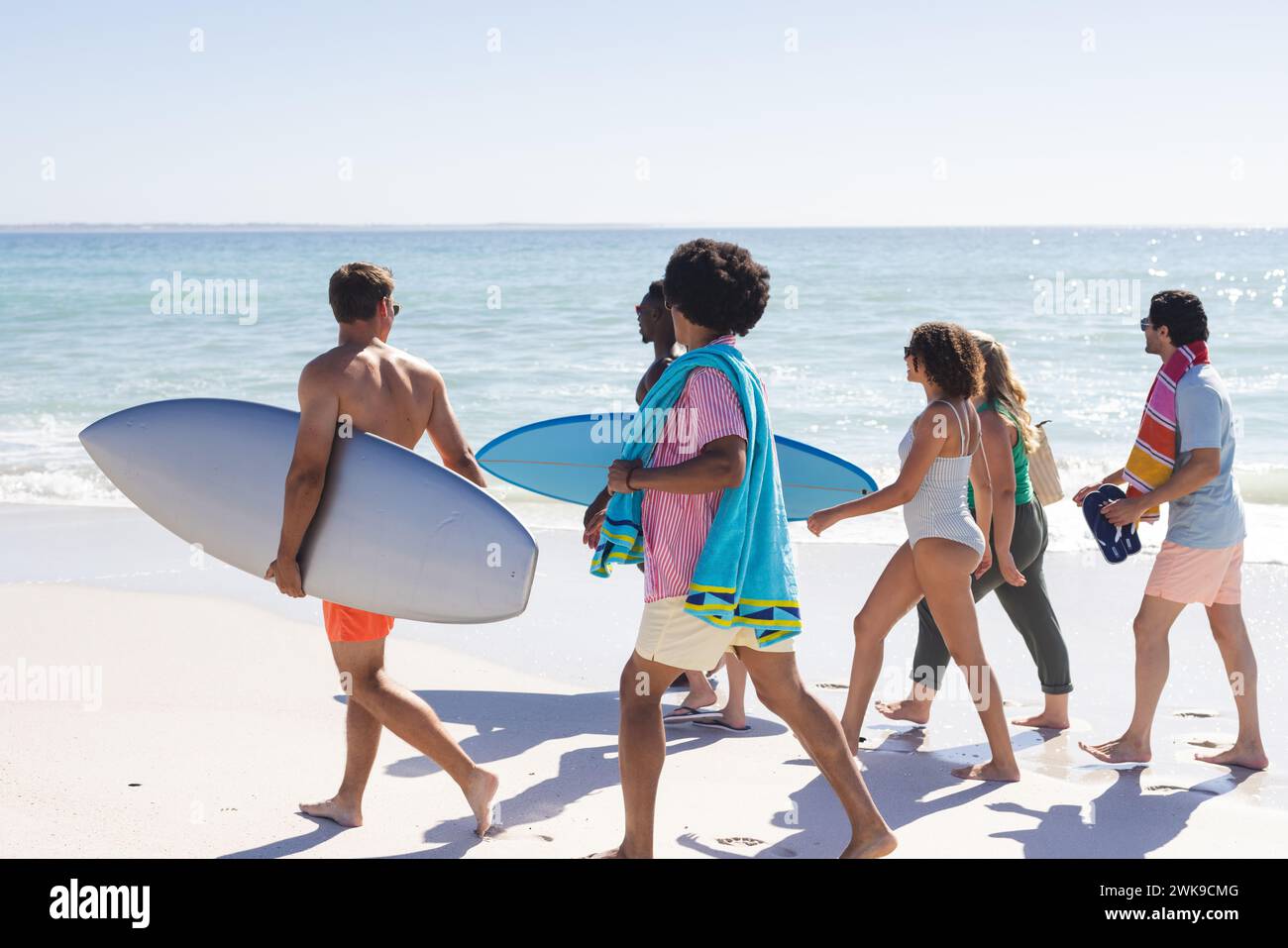 Diversi amici si dirigono a fare surf con le loro tavole in una giornata di sole sulla spiaggia Foto Stock