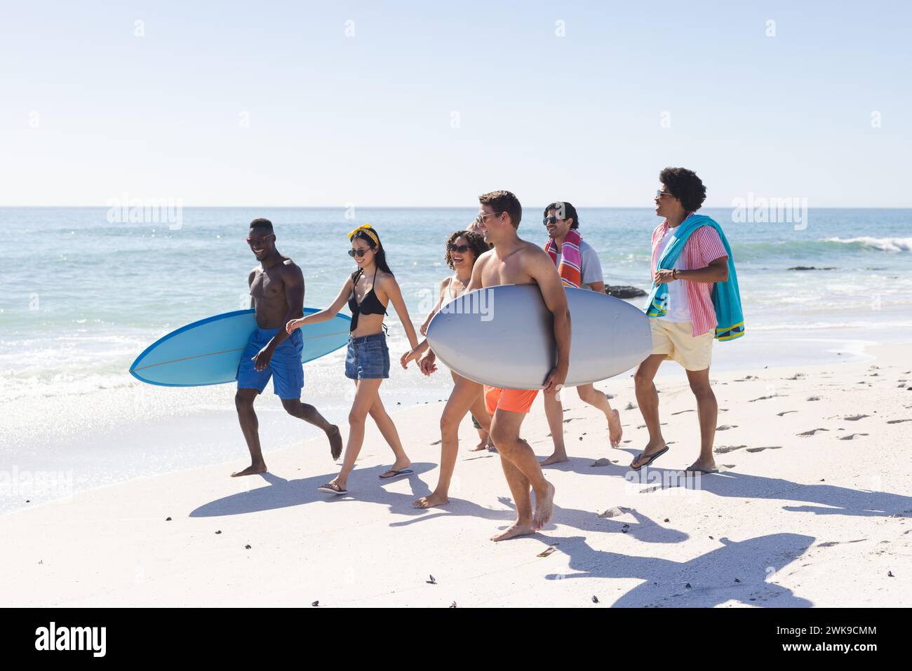Diversi gruppi di amici portano tavole da surf su una spiaggia soleggiata Foto Stock