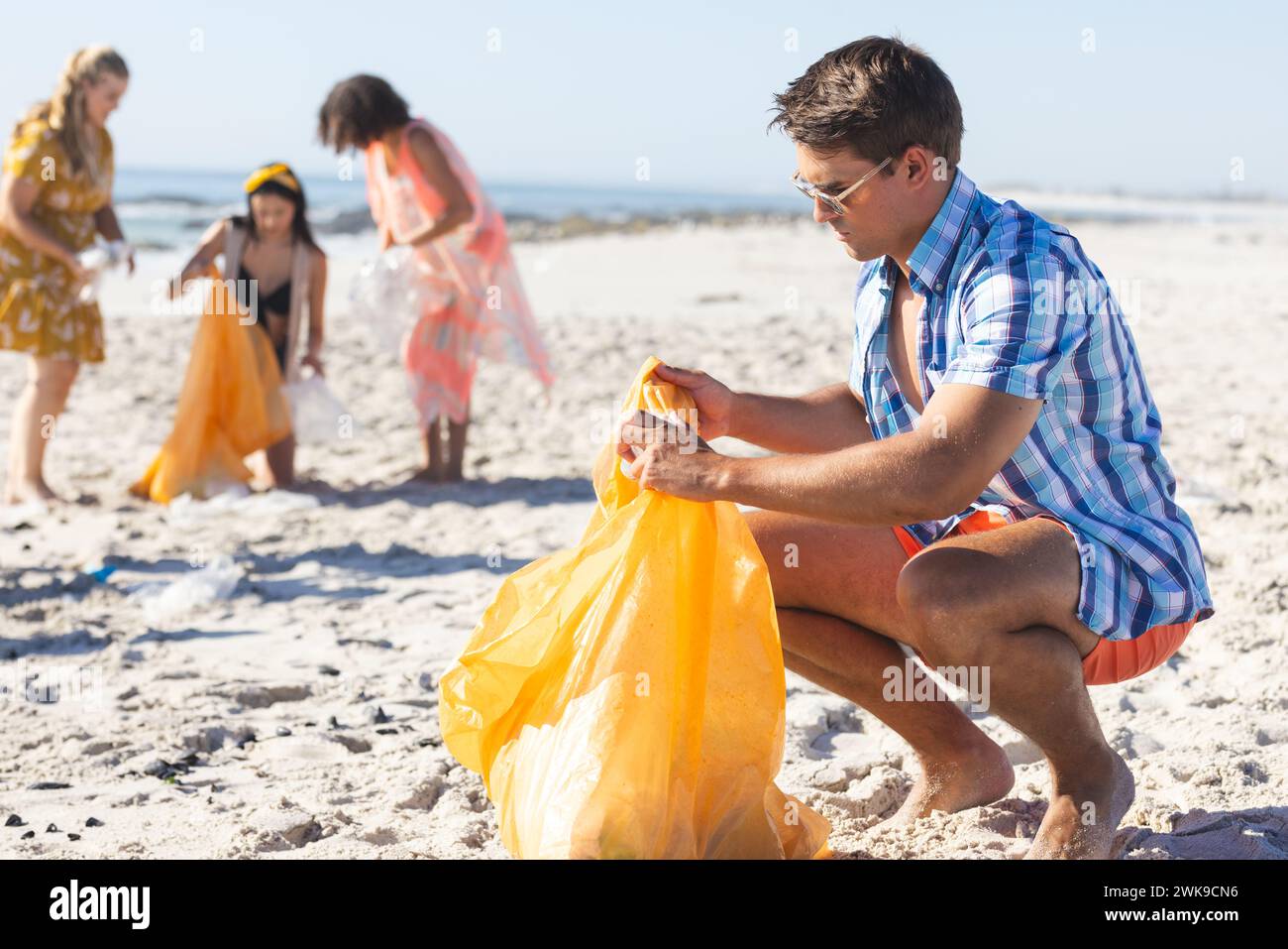 Un gruppo eterogeneo di amici partecipa alla pulizia della spiaggia, raccogliendo rifiuti Foto Stock