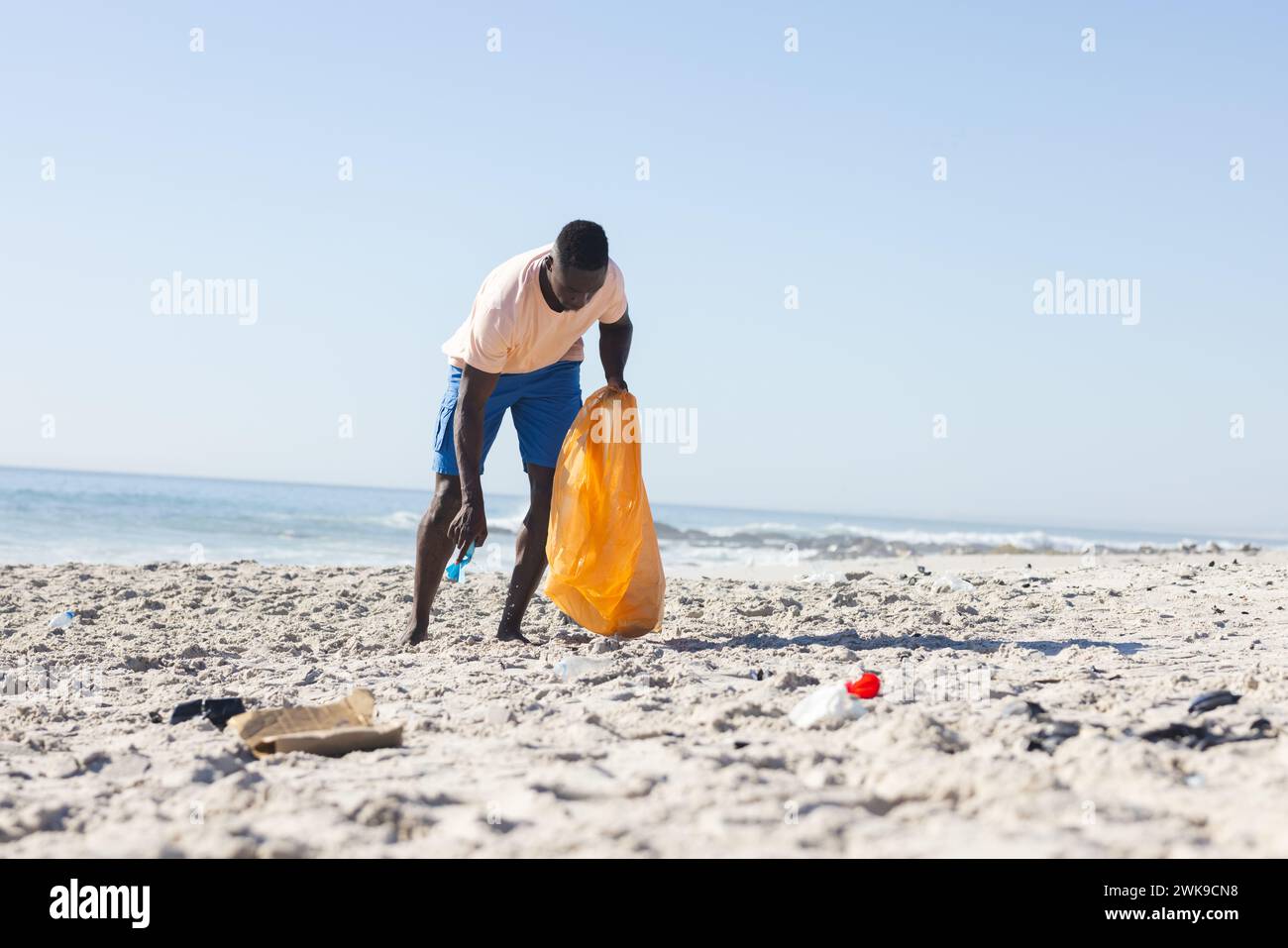 Un giovane afroamericano pulisce una spiaggia, raccogliendo spazzatura, con spazio di copia Foto Stock