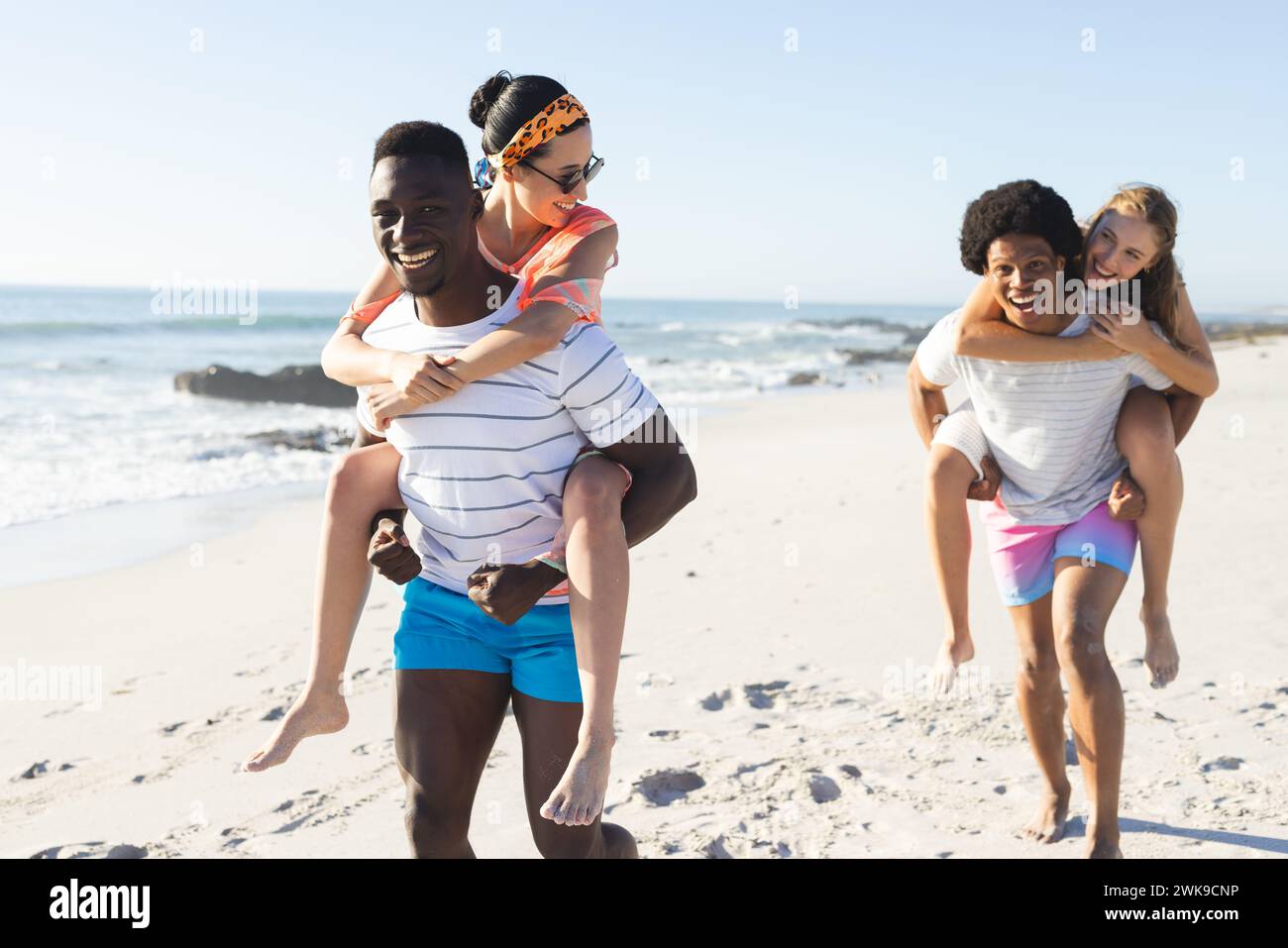 I diversi amici si divertono a fare giri in piggyback su una spiaggia soleggiata Foto Stock