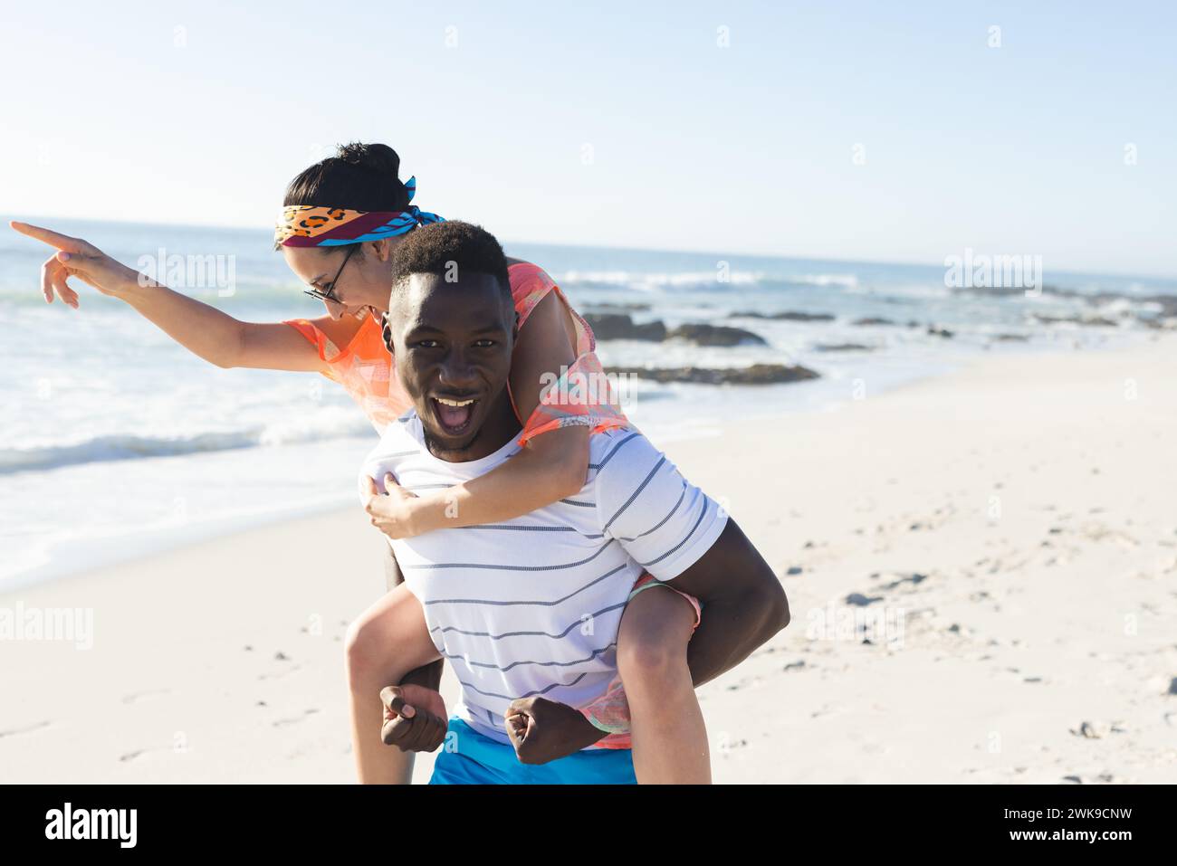 Giovane donna birazziale e uomo afroamericano si godono un momento giocoso sulla spiaggia Foto Stock