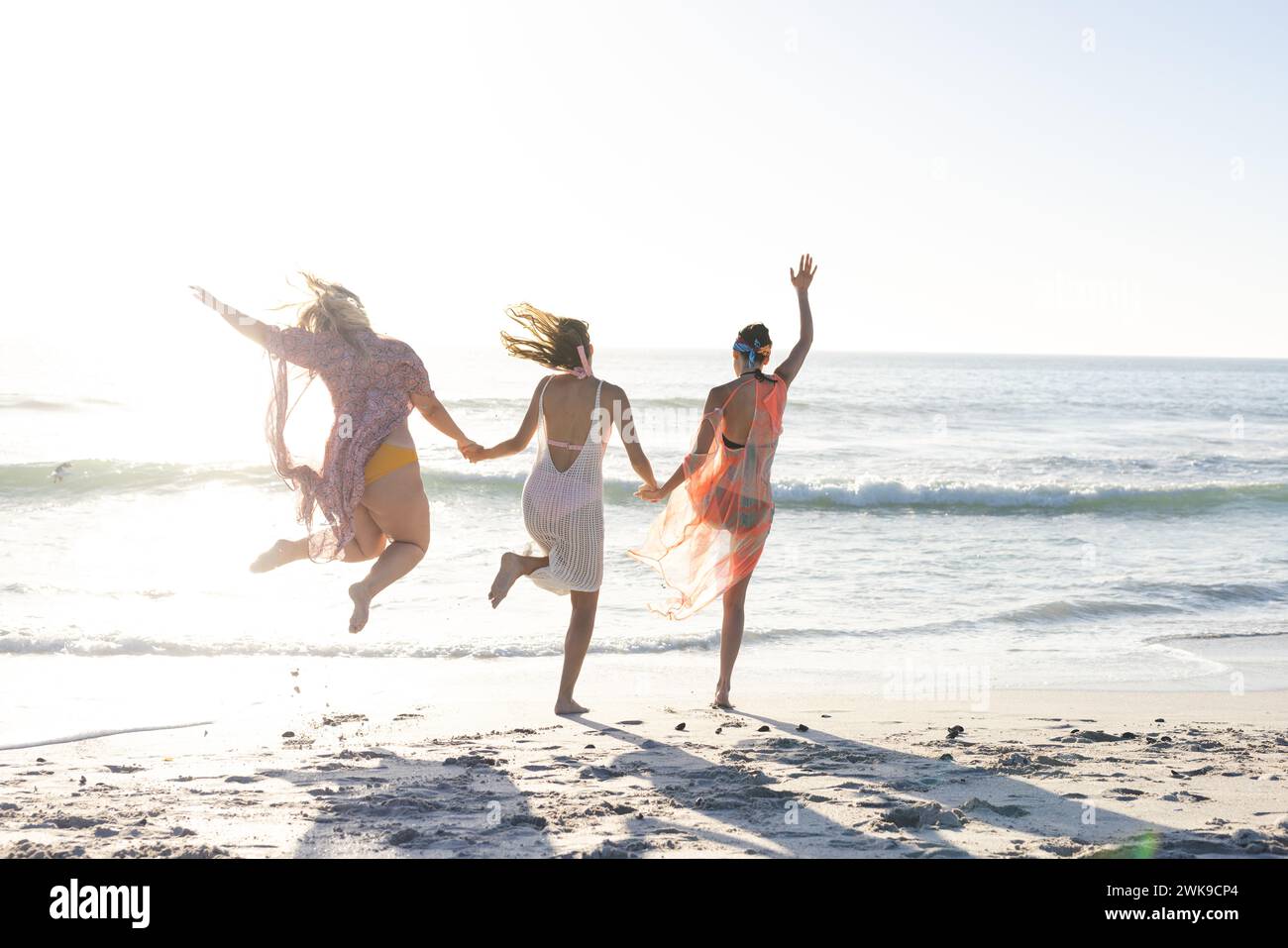 Tre giovani donne si divertono a fare un salto spensierato su una spiaggia soleggiata Foto Stock