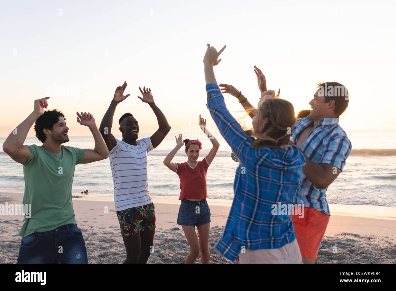 Gruppi eterogenei di amici si godono un tramonto sulla spiaggia, con spazio per fotocopie Foto Stock