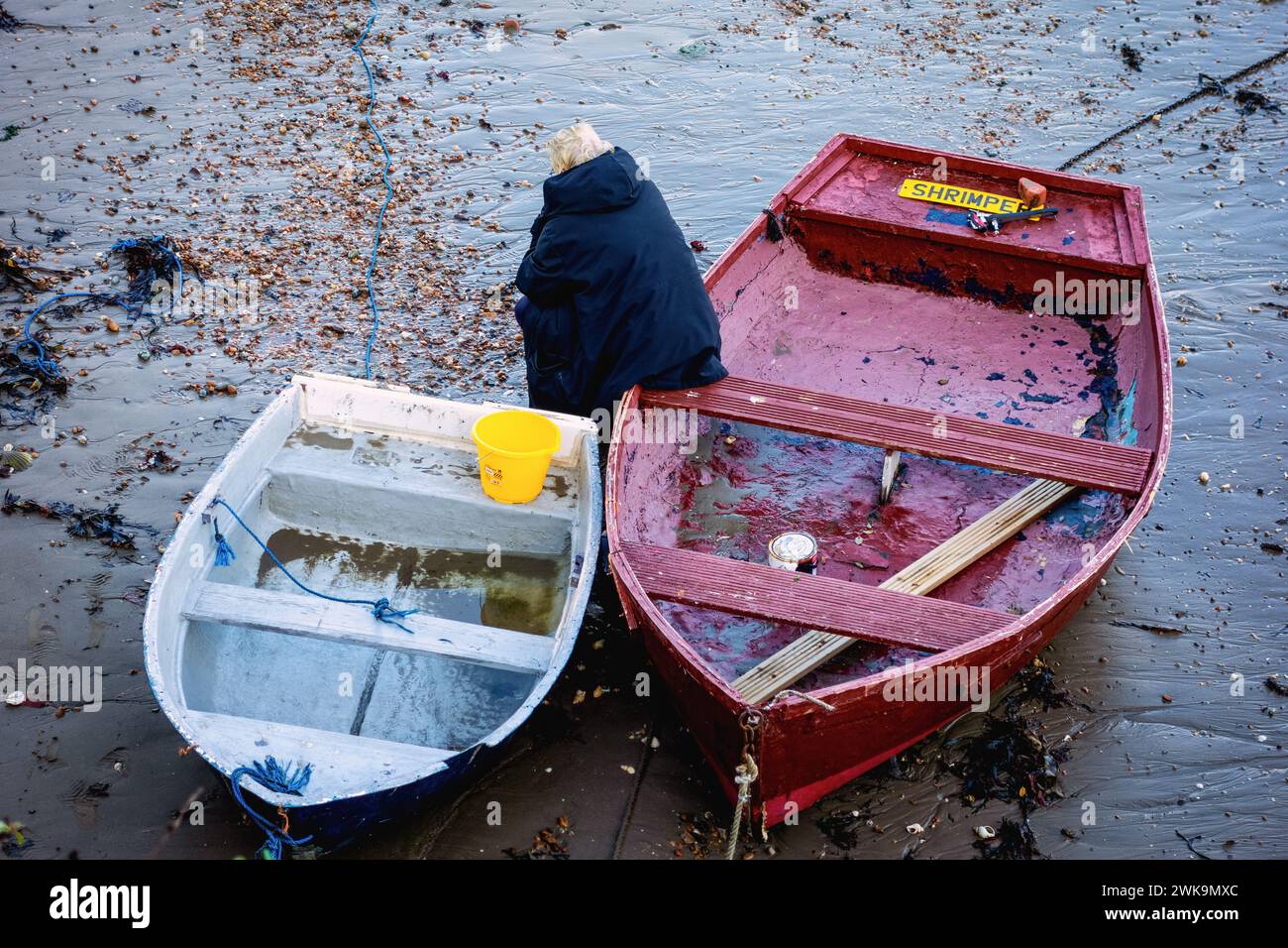 Persona seduta sul bordo di una barca a remi nel porto di Folkestone con la bassa marea Foto Stock