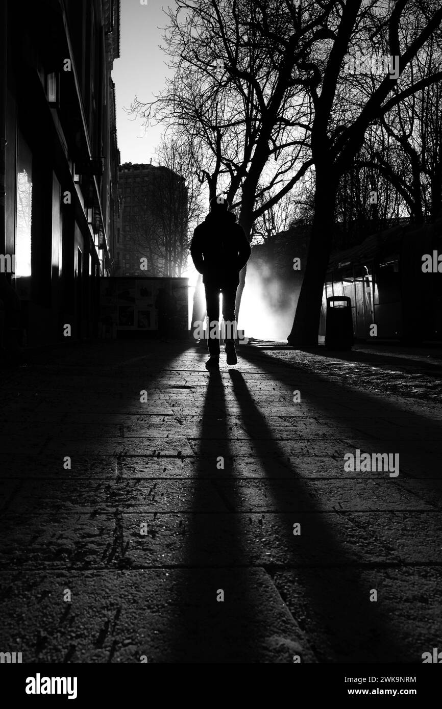 Una persona cammina su una strada illuminata dal sole in scala di grigi Foto Stock