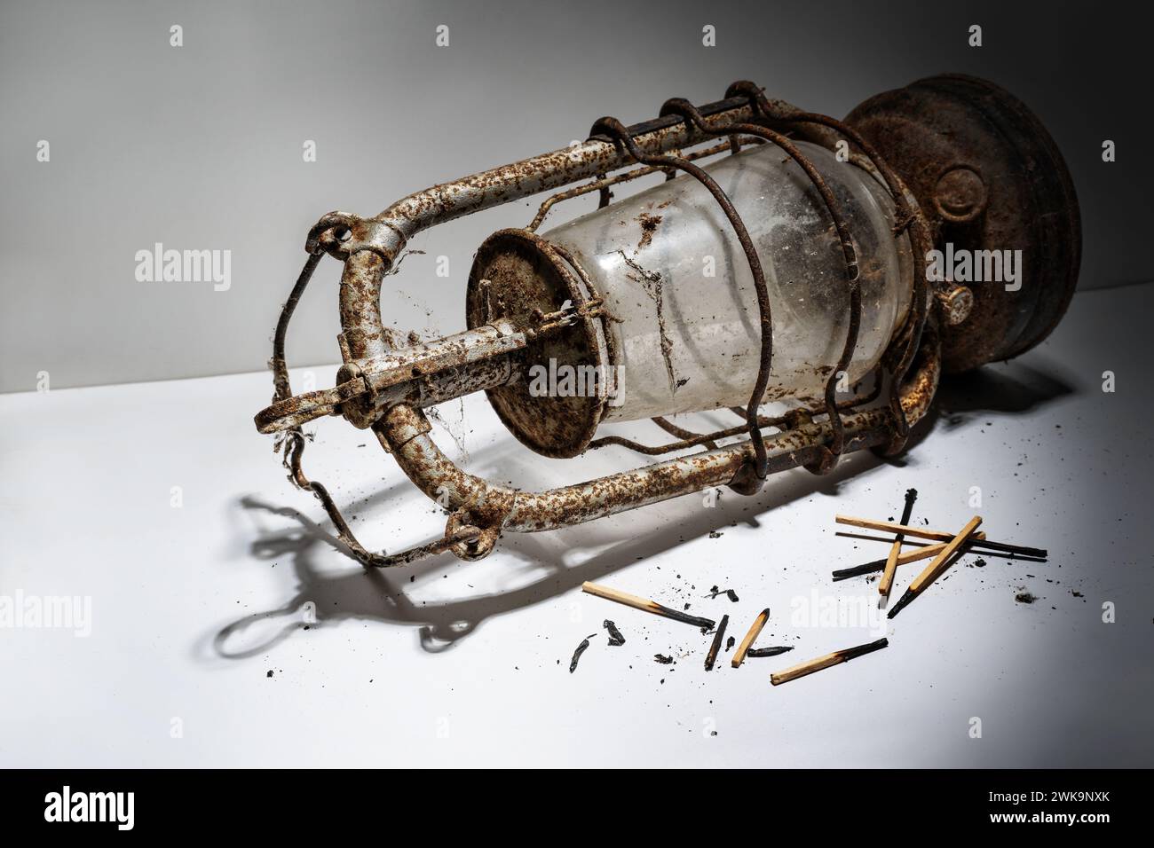 Vecchia lampada a cherosene arrugginita e fiammiferi bruciati adagiati su sfondo grigio, simboleggiando concetti obsoleti che non sono più in linea con i tempi, copia Foto Stock