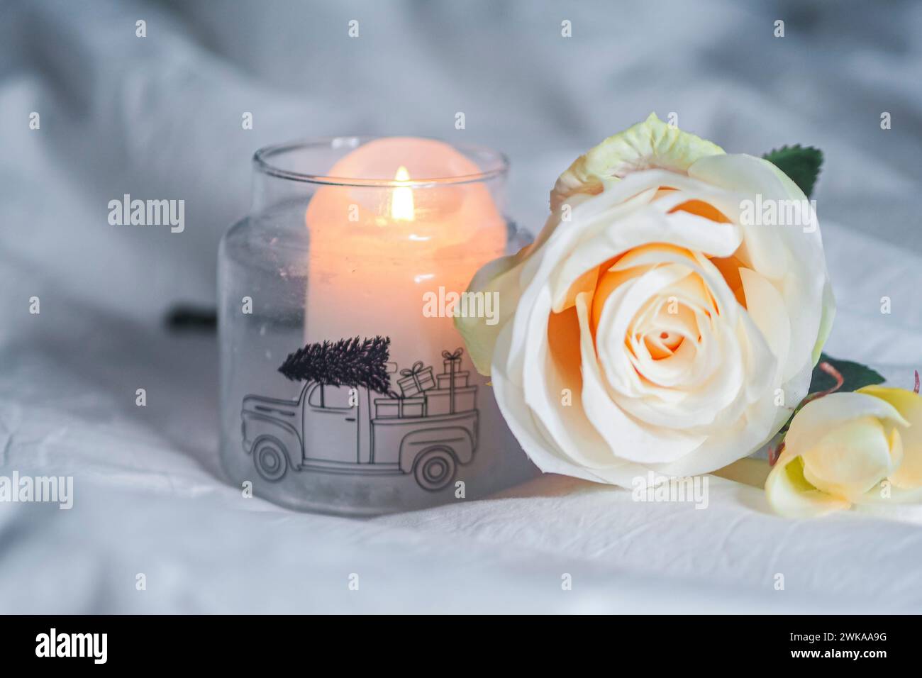 Una candela e una rosa su un letto con cuscini Foto Stock