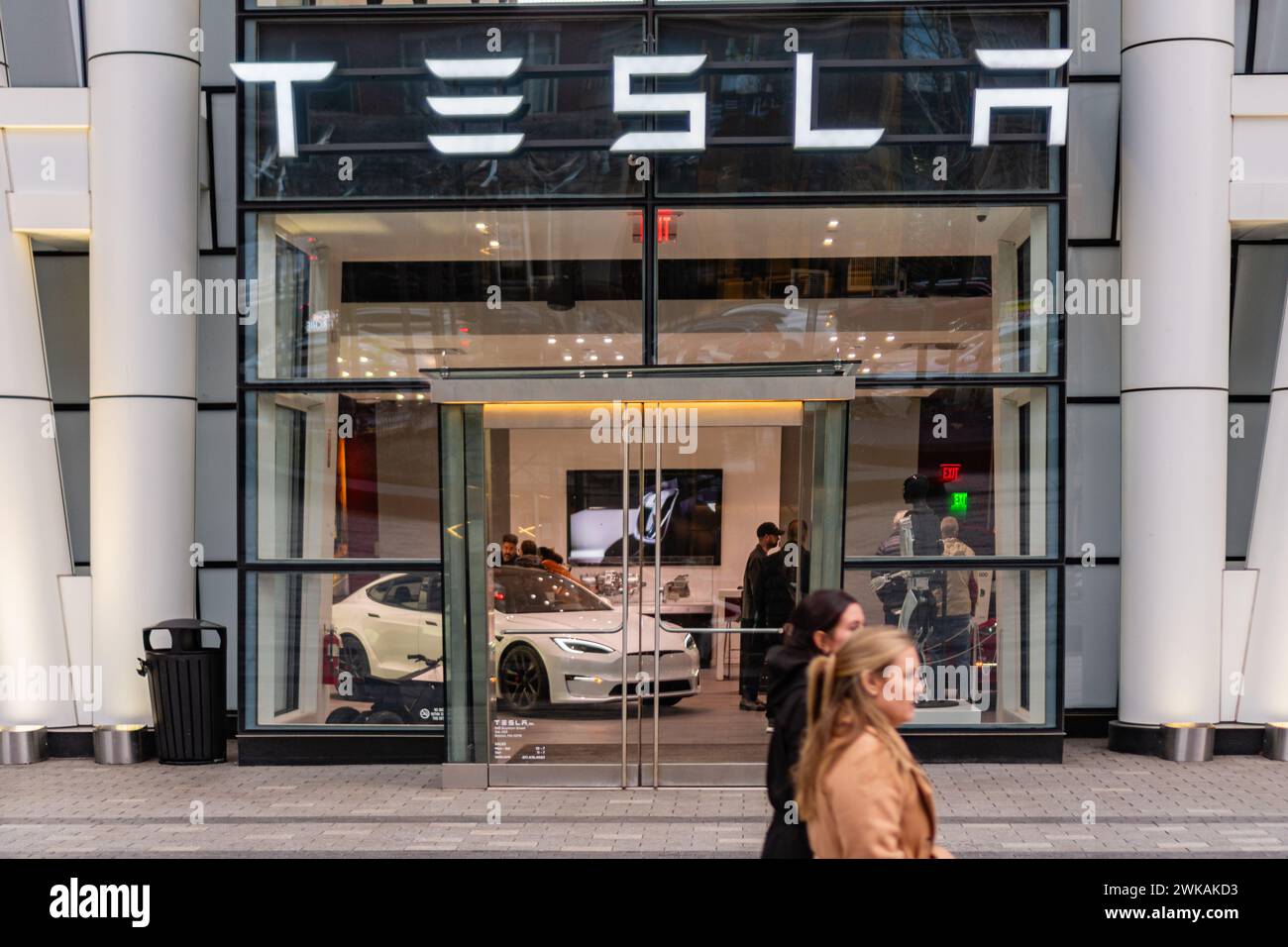 Boston, ma, Stati Uniti - 15 gennaio 2024: Le persone passano accanto all'ingresso dello showroom di auto elettriche Tesla con i clienti che guardano i veicoli. Foto Stock