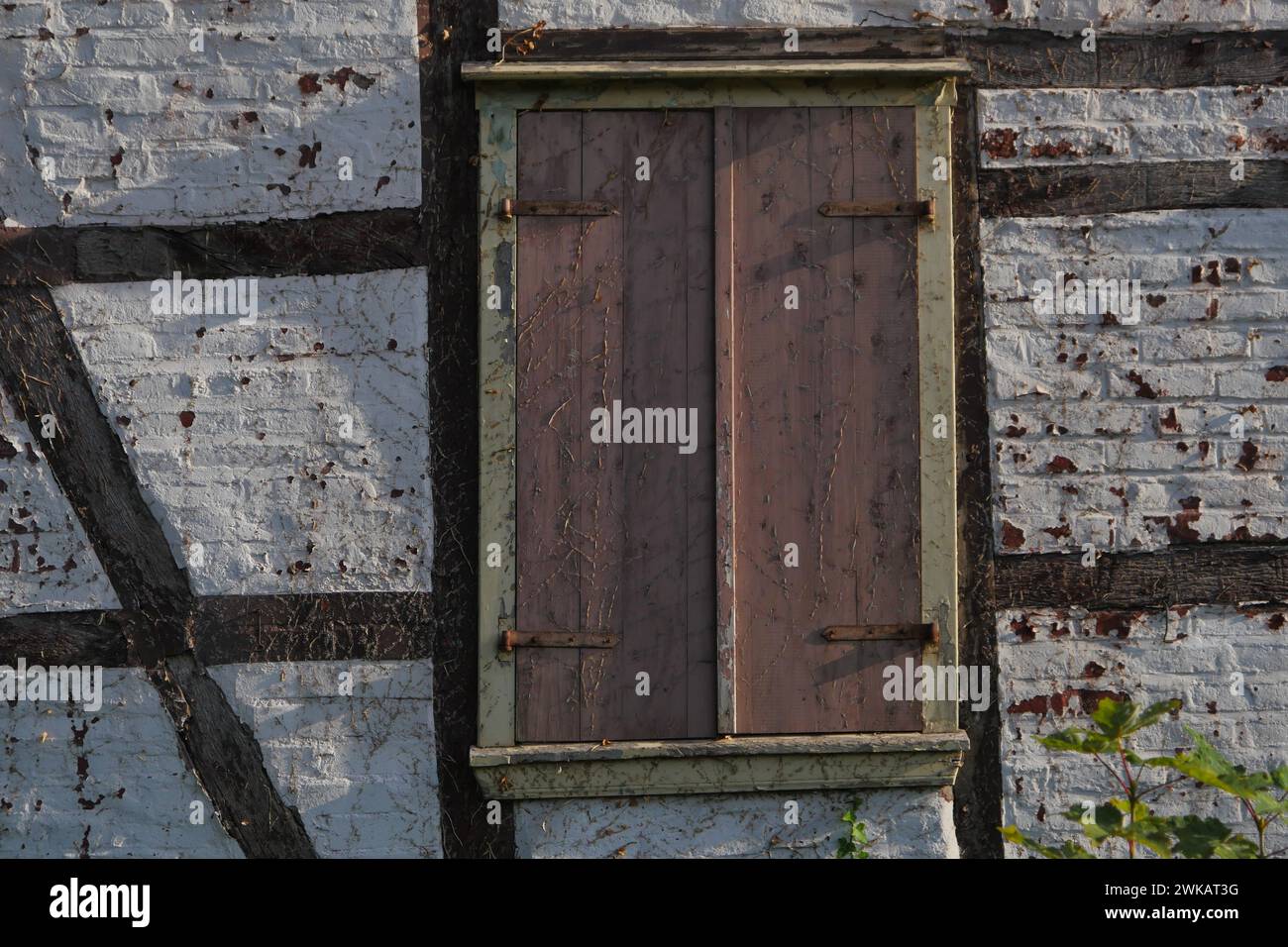 Dettagli di una casa per metà in legno che necessita di ristrutturazione, le persiane sono chiuse, i raccordi sono arrugginiti, pareti di pietra bianca, la vernice si sta staccando Foto Stock