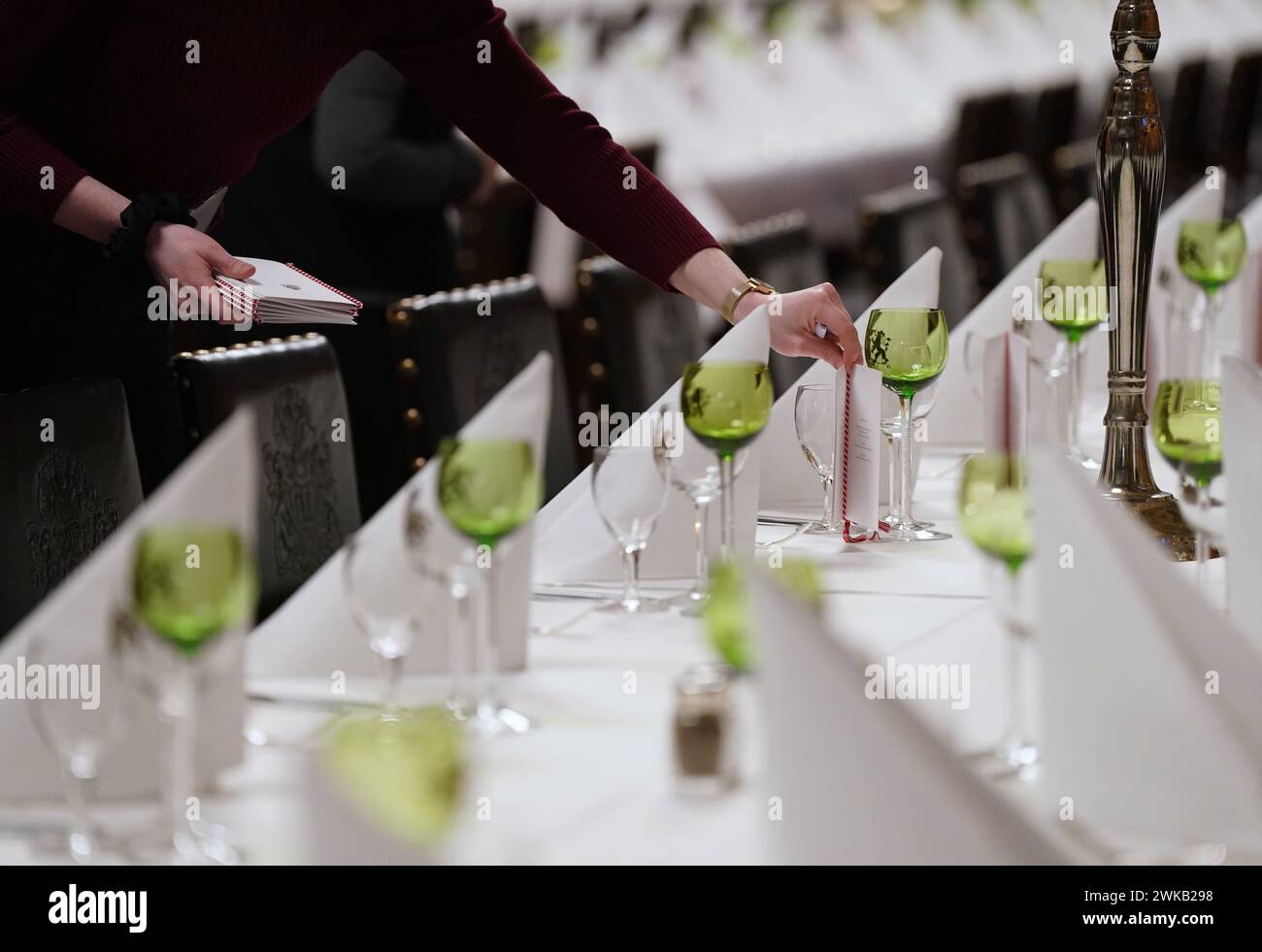 Amburgo, Germania. 19 febbraio 2024. Un membro del personale mette le carte del menu sui tavoli durante i preparativi finali per il tradizionale pasto Matthiae del Senato di Amburgo nella grande sala da ballo del municipio. Il primo ministro della Repubblica di Estonia, Kallas, e il cancelliere federale Scholz dovrebbero partecipare al pasto di Matthiae come ospiti d'onore. Crediti: Marcus Brandt/dpa/Alamy Live News Foto Stock