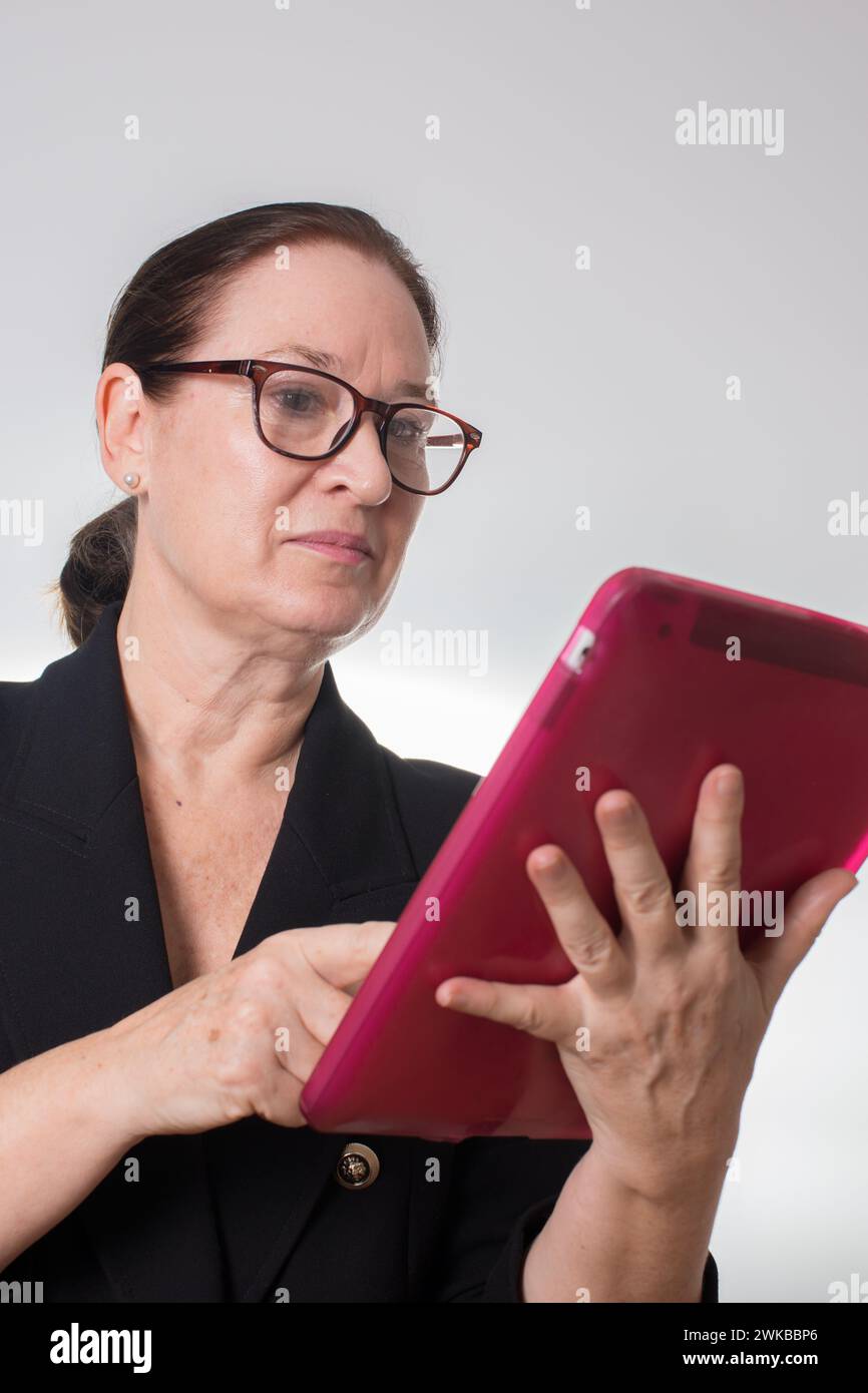 Donna d'affari matura con occhiali che reggono un tablet digitale. Vista dal basso. Sfondo bianco Foto Stock