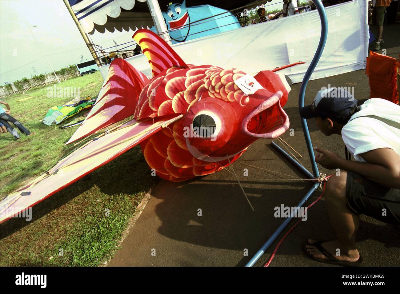 Un uomo sta prestando attenzione a un aquilone tridimensionale creato sotto forma di pesce durante il Jakarta International Kite Festival del 2004 che si è tenuto il 9-11 luglio a Carnival Beach ad Ancol Dreamland, a nord di Giacarta, Giacarta, Indonesia. Foto Stock