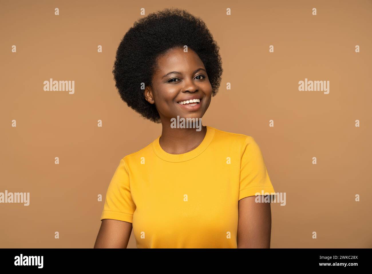 Donna nera allegra e sincera sorridente, guardando la macchina fotografica, isolata in camicia gialla su sfondo beige Foto Stock