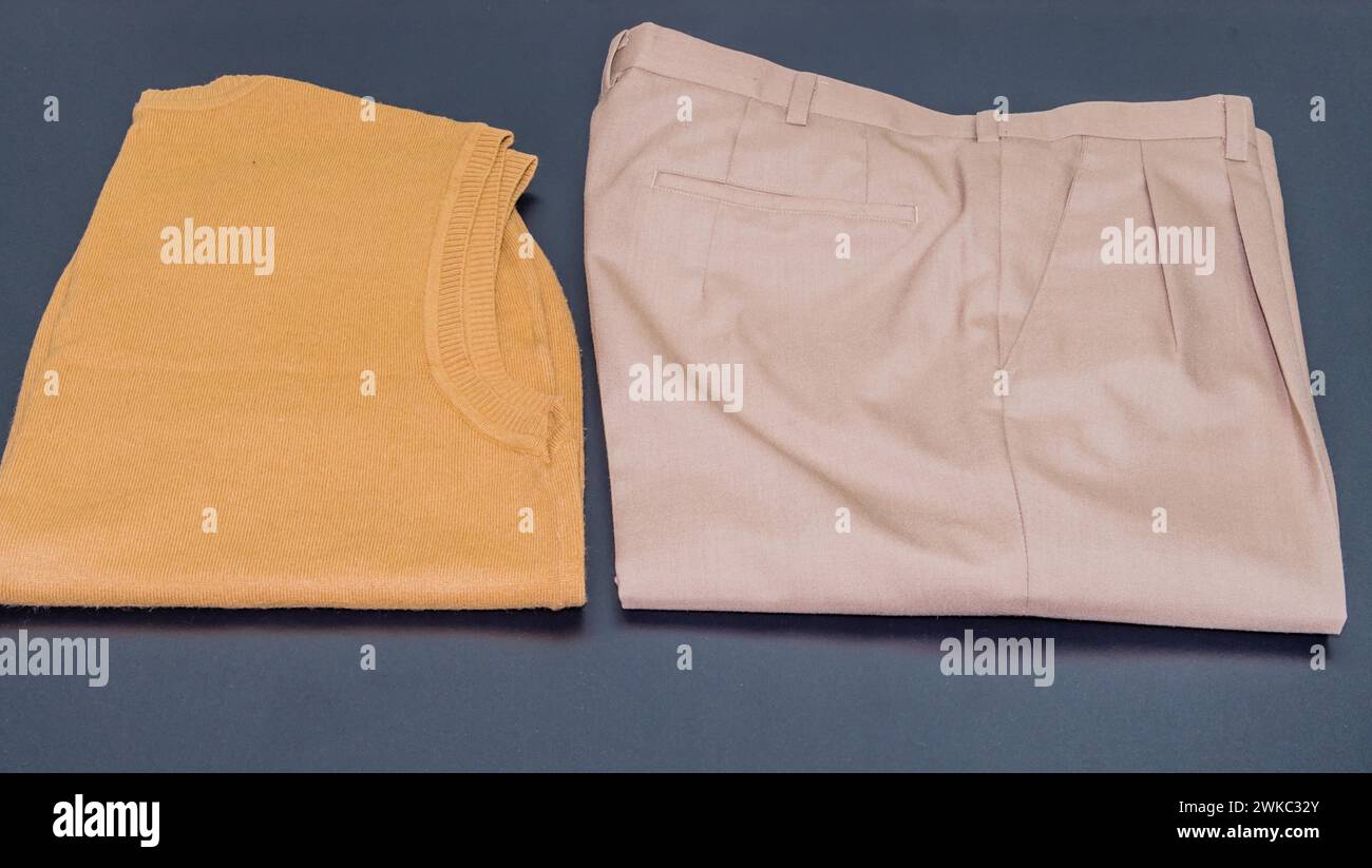 Pullover senza maniche marrone accanto a un paio di pantaloni beige a pieghe su sfondo nero Foto Stock