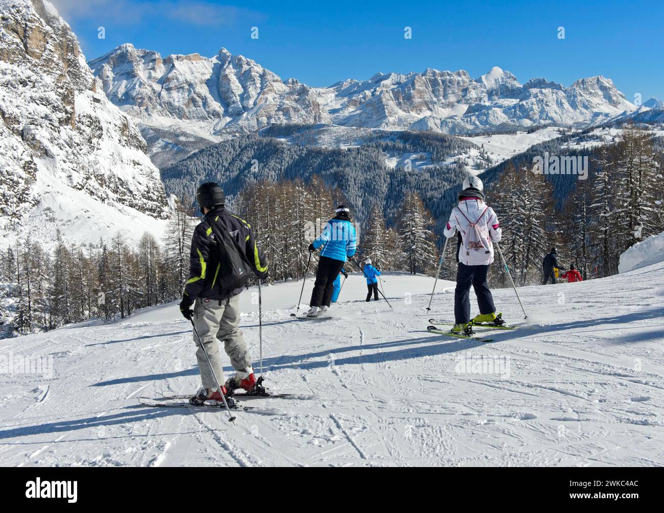 Sciatori su pista di fronte alla catena montuosa innevata delle Dolomiti, località sciistica di Colfosco, Colfosco, area sciistica dell'alta Badia Foto Stock