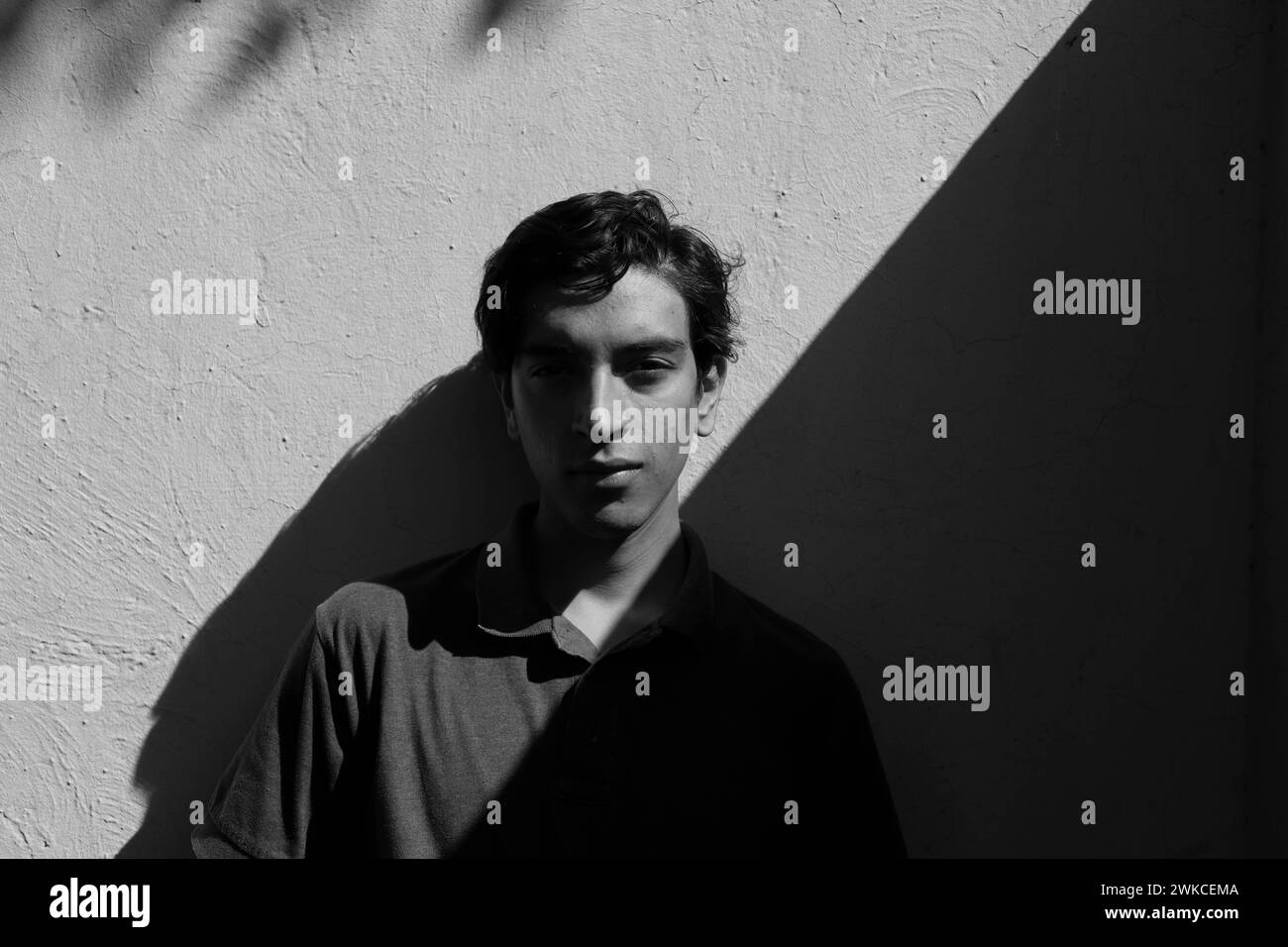 Giovane uomo contro un muro con un'illuminazione spettacolare e un volto senza espressioni. Foto Stock Giovane uomo contro un muro con un'illuminazione spettacolare e un volto senza espressioni. Foto Stock