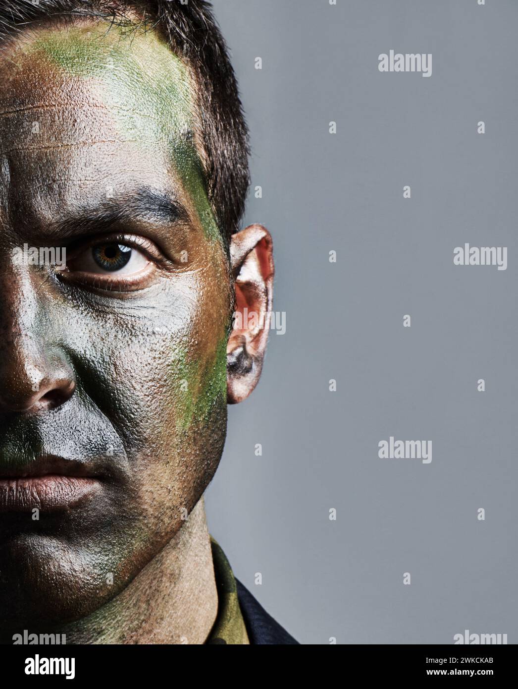 Uomo, ritratto e soldato con facciale dipinto per camuffamento, guerra militare o battaglia su sfondo grigio. Primo piano di uomini, esercito o.. Foto Stock