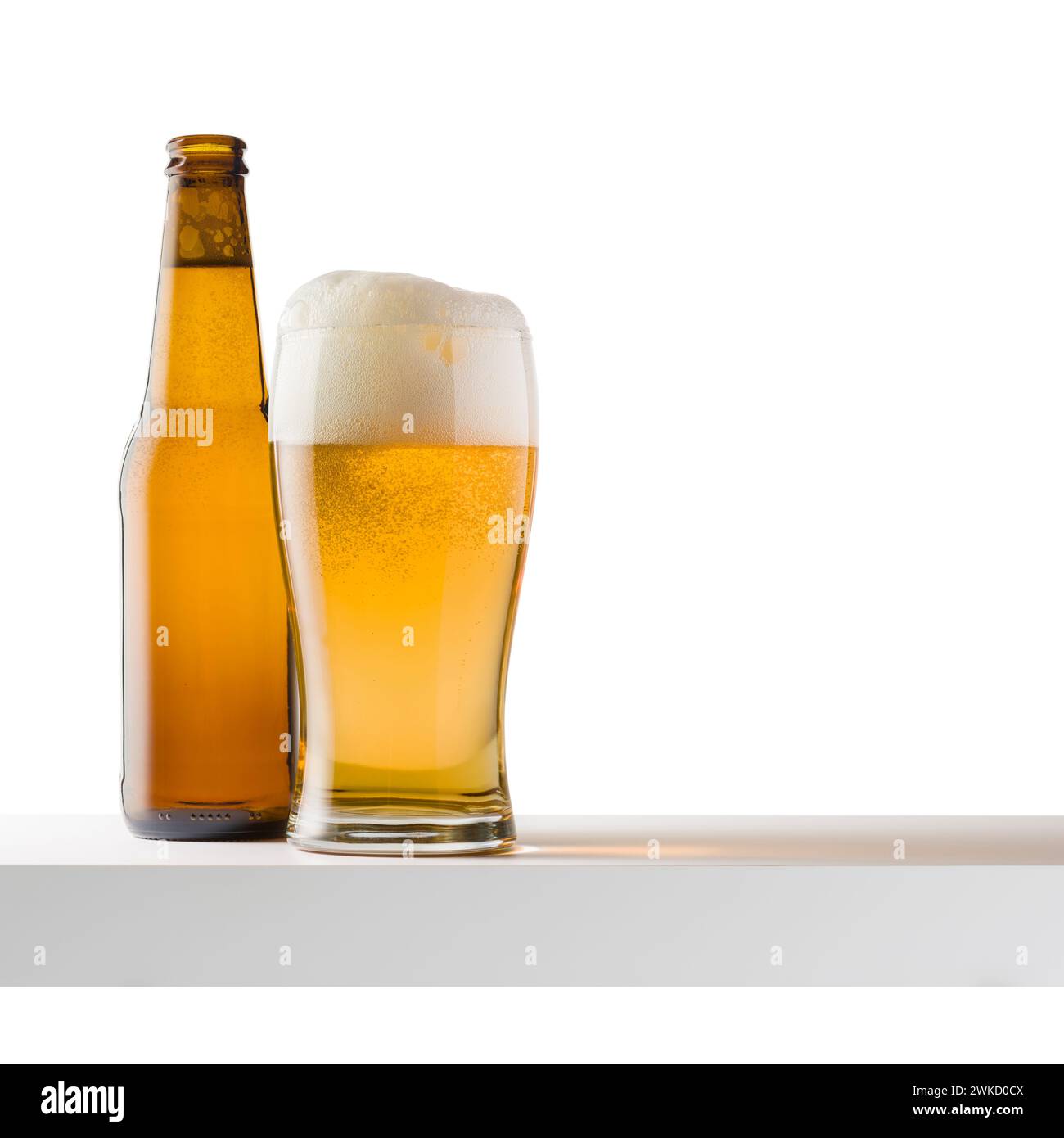 Bicchiere di birra bionda con bottiglia su ripiano bianco, isolato su sfondo bianco. Foto Stock