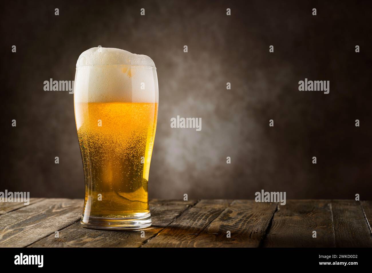 bicchiere di birra bionda con schiuma su sfondo scuro. Foto Stock