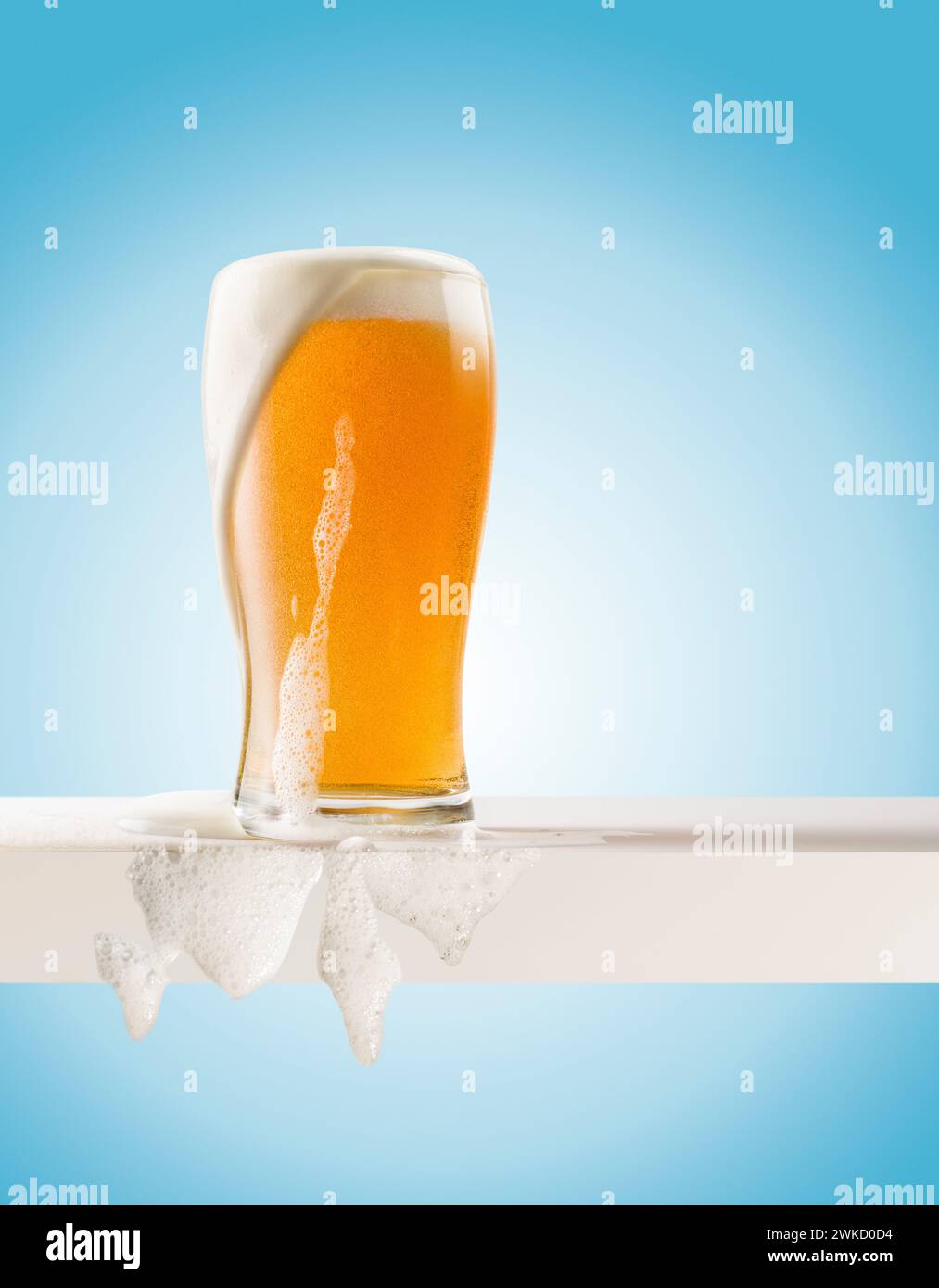 Bicchiere di birra bionda con schiuma su ripiano bianco su sfondo blu. Foto Stock