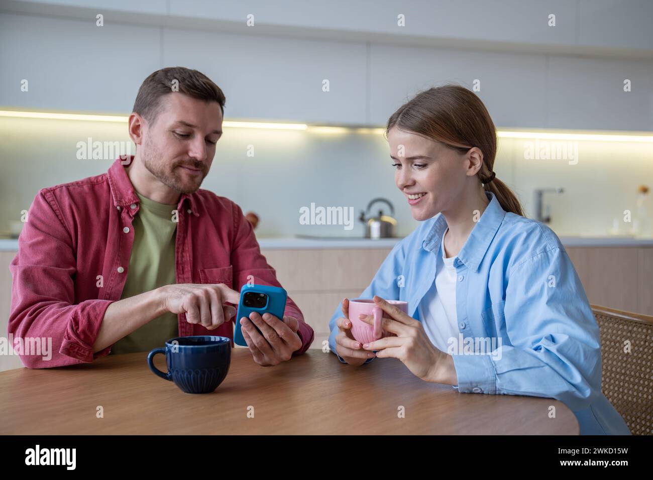 Una coppia di famiglie che ama bere un caffè guardando le foto sul cellulare, trascorrendo del tempo insieme a casa. Foto Stock