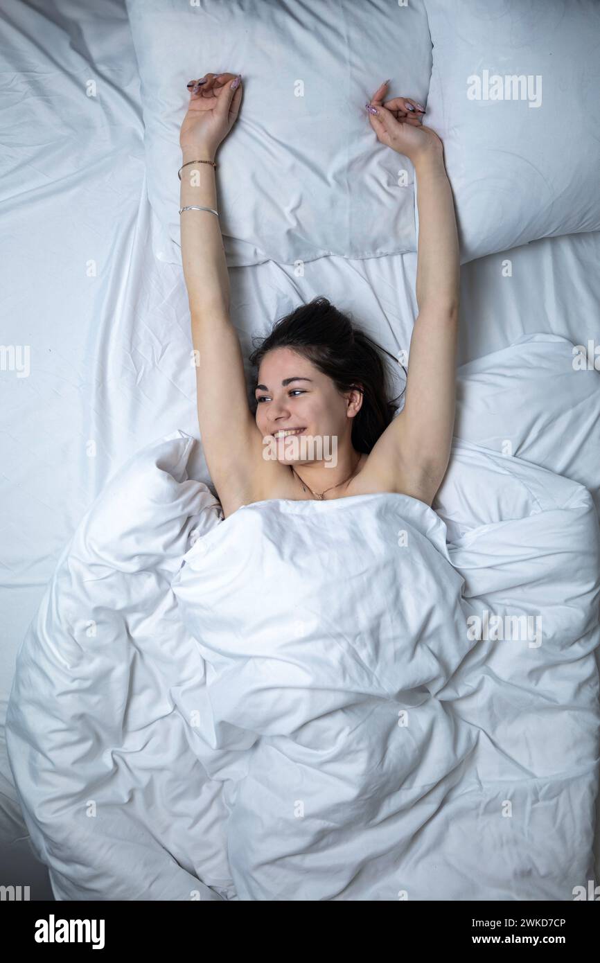 Una bella ragazza sta dormendo in un letto con un lenzuolo bianco. Foto Stock