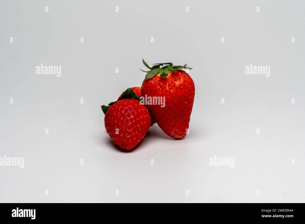 , Food, Deutschland, 20.02.2024, Drei reife Erdbeeren mit lebendiger roter Farbe und Grünen Blättern auf weißem Hintergrund. Foto Stock