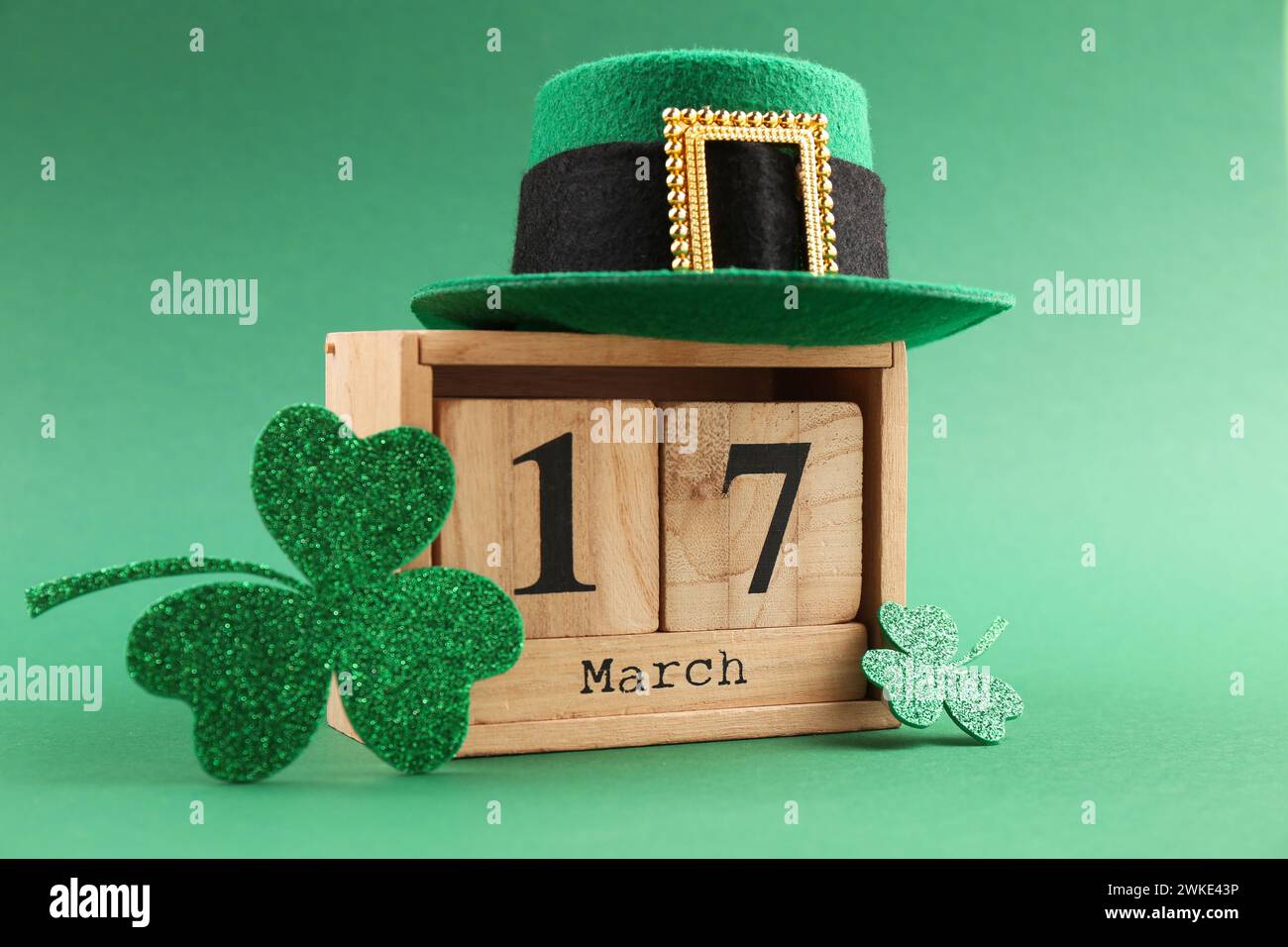 St Giorno di Patrick - 17 marzo. Calendario a blocchi di legno, cappello di leprecaun e foglie di trifoglio decorativo su sfondo verde Foto Stock
