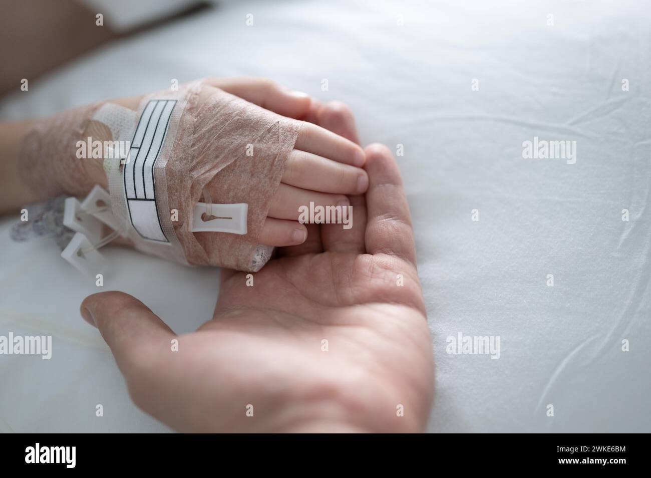 Mano adulto tenere il palmo del bambino in fondo del letto di ospedale vista ravvicinata Foto Stock