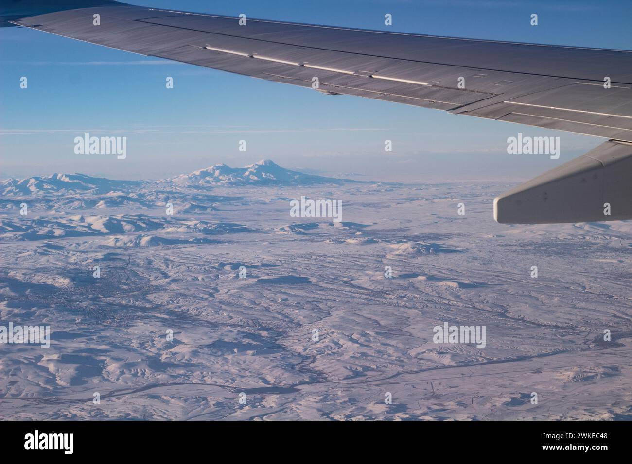 Il cielo con le nuvole e le montagne nella neve. Foto scattata da un aereo. Ala di un aereo nel cielo. Foto Stock