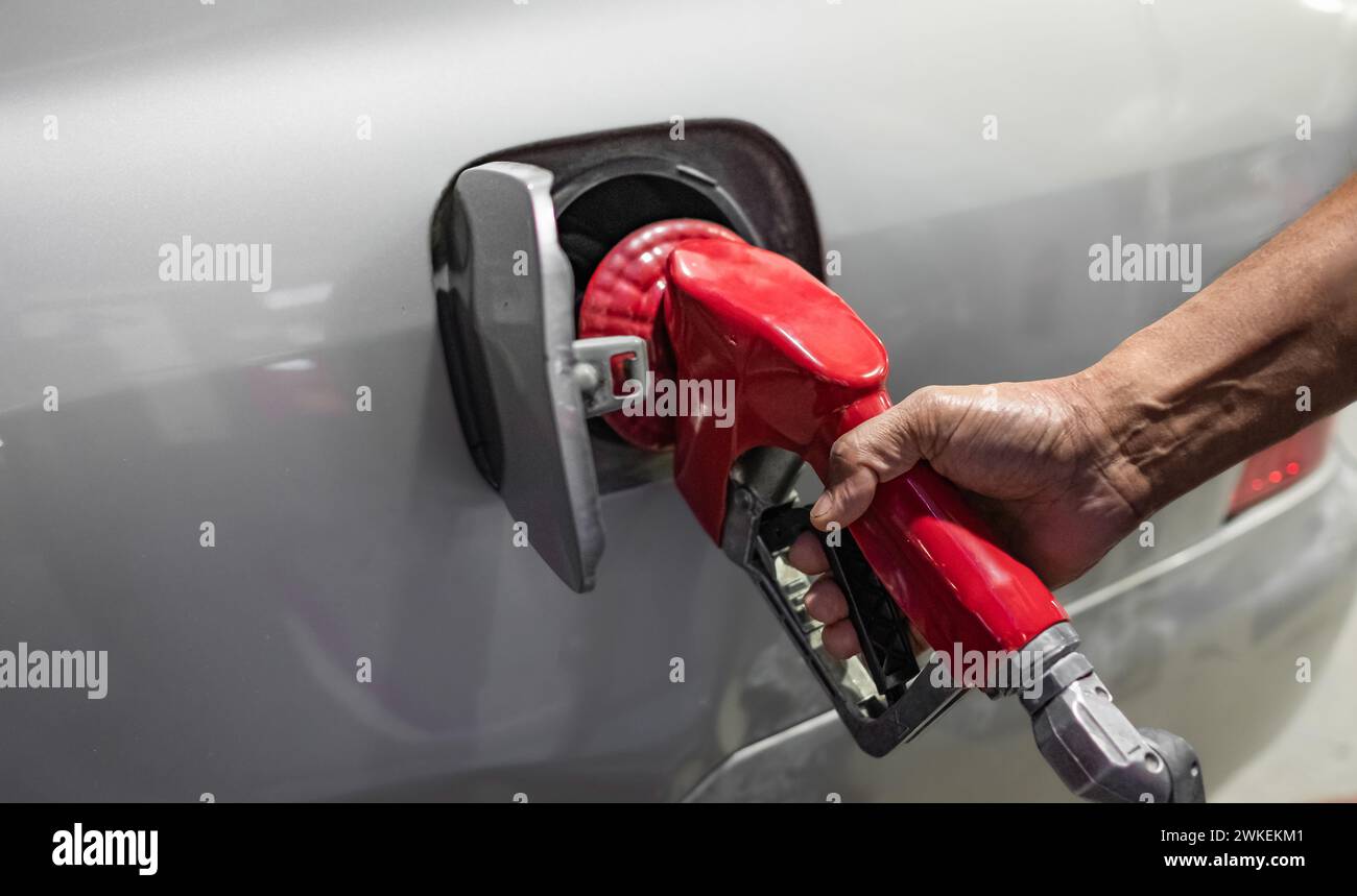 Primo piano della mano di un uomo che usa una pompa di benzina per riempire la sua auto di carburante. Un uomo riempie la sua auto con una benzina al distributore di benzina. Messa a fuoco selettiva, copia Foto Stock