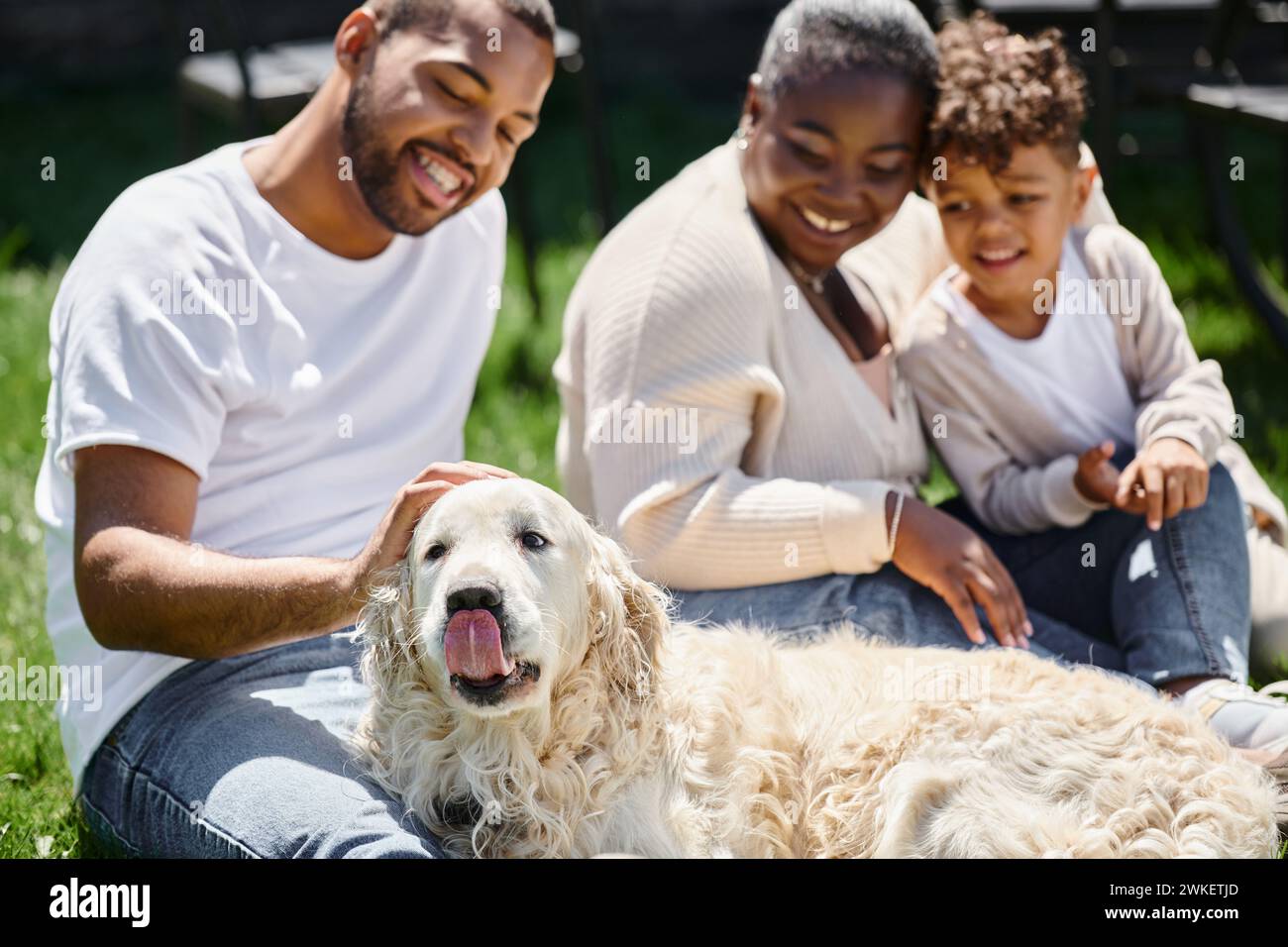 momenti in famiglia di genitori afroamericani e figli sorridenti e seduti sul prato e accarezzare il cane Foto Stock