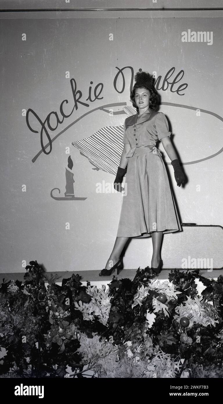 Anni '1950, storica, un'elegante giovane donna che posa su un palco con un abito alla moda "Jackie Nimble" lungo un vitello + guanti e cappello. Foto Stock