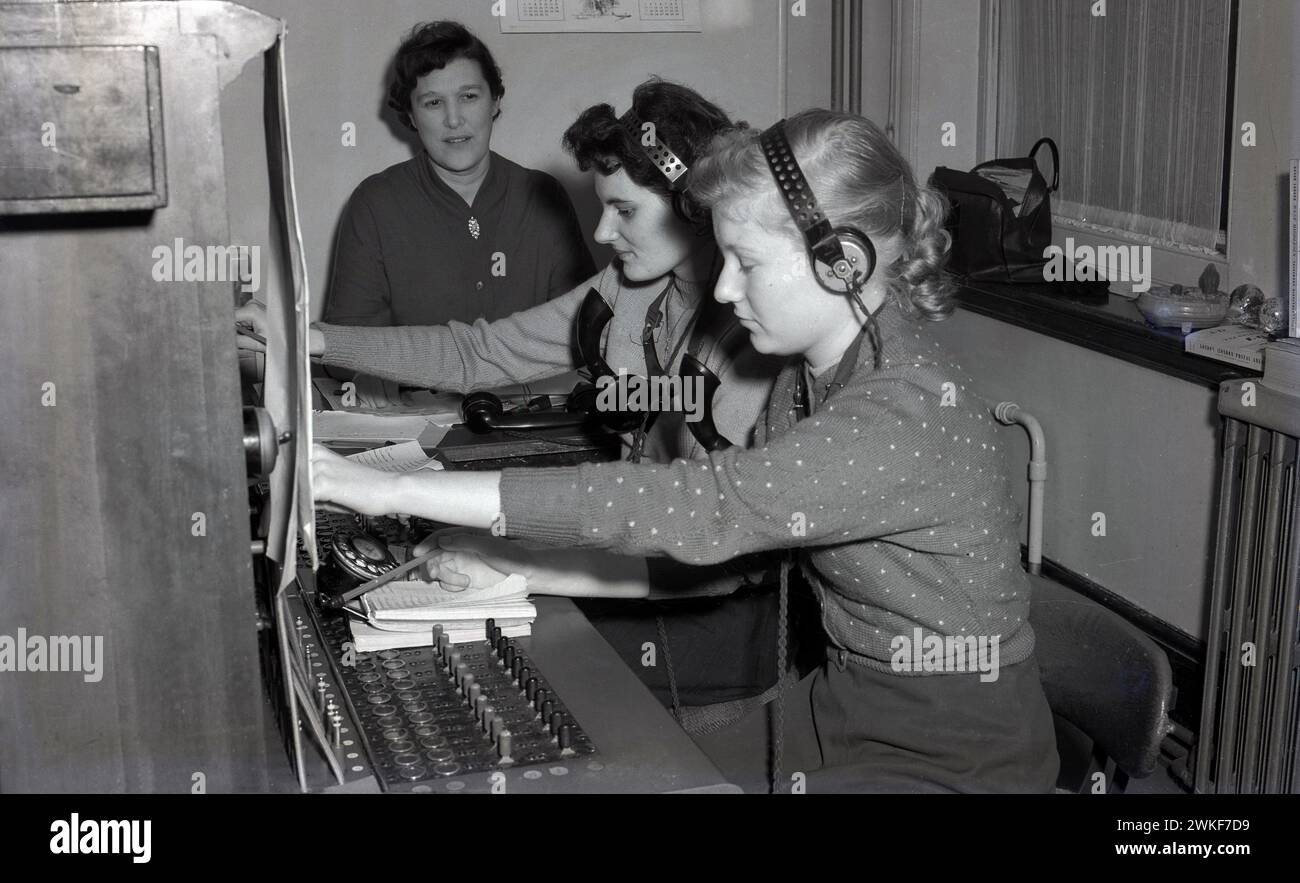 1957, storico, due ragazze sedute con le cuffie, che imparano a gestire un centralino telefonico, sono supervisionate da una donna seduta accanto a loro, Londra, Inghilterra, Regno Unito. Foto Stock