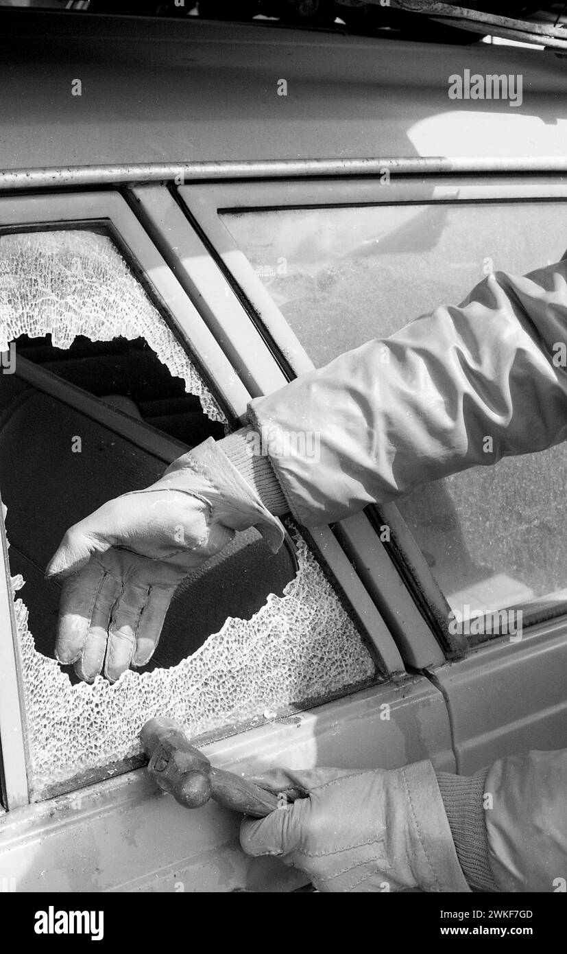Anni '1970, storico, furto d'auto, una mano con i guanti che butta fuori il vetro frantumato del finestrino laterale di un'auto, un martello tenuto in un'altra mano con i guanti, Inghilterra, Regno Unito. Foto Stock