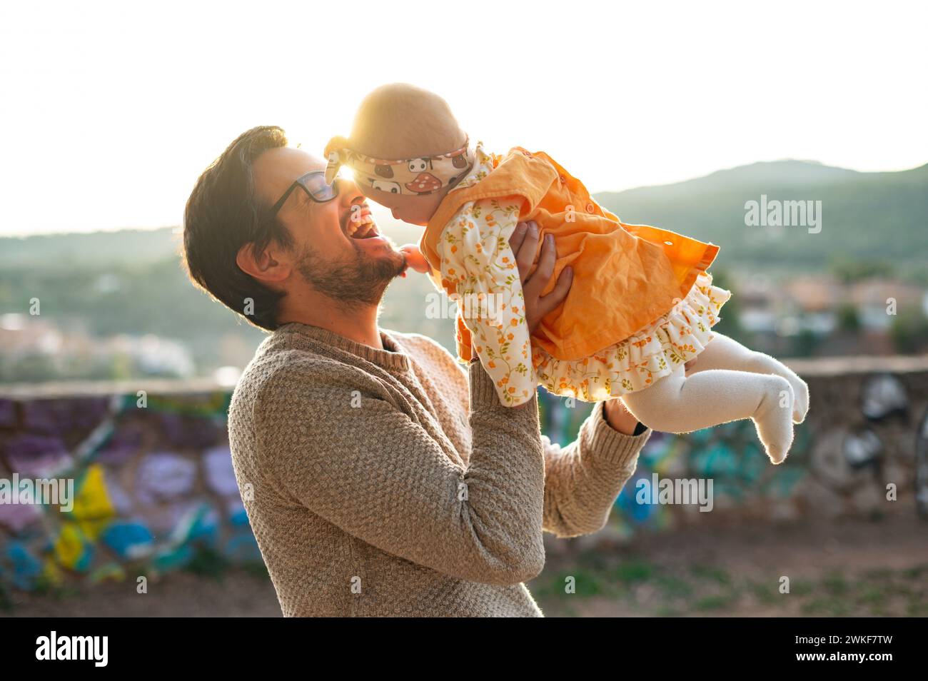 Un giovane e allegro papà solleva la sua bambina in aria durante un bellissimo tramonto, condividendo un momento di felicità. Foto Stock