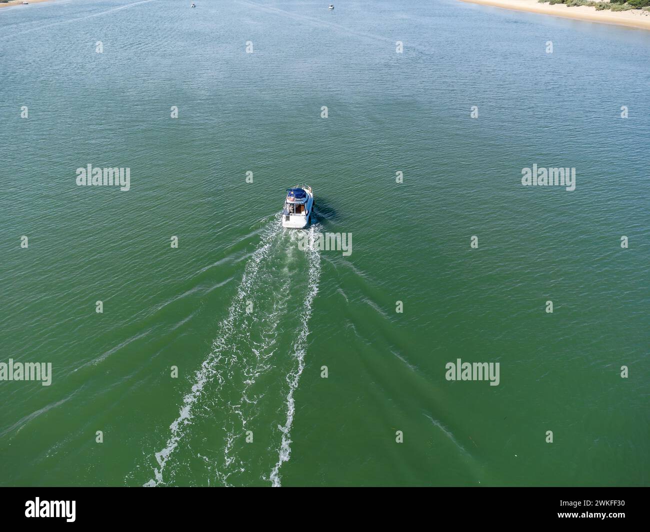 Vista aerea con droni di una barca a motore che naviga nel fiume Piedras tra il villaggio sulla spiaggia di El Portil e la riva di sabbia di la Flecha Foto Stock
