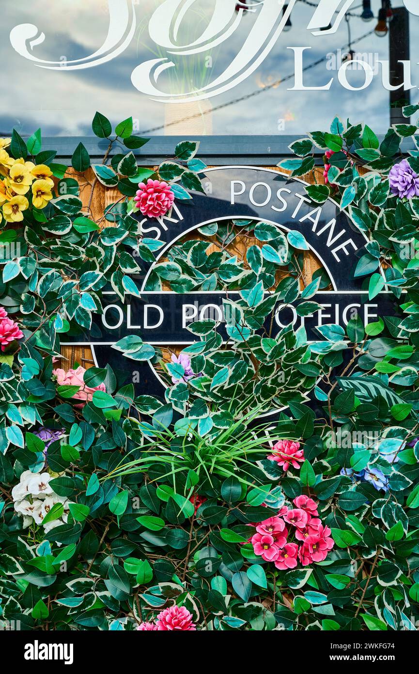 Vecchio cartello dell'ufficio postale ricoperto di fiori di plastica e fogliame Foto Stock
