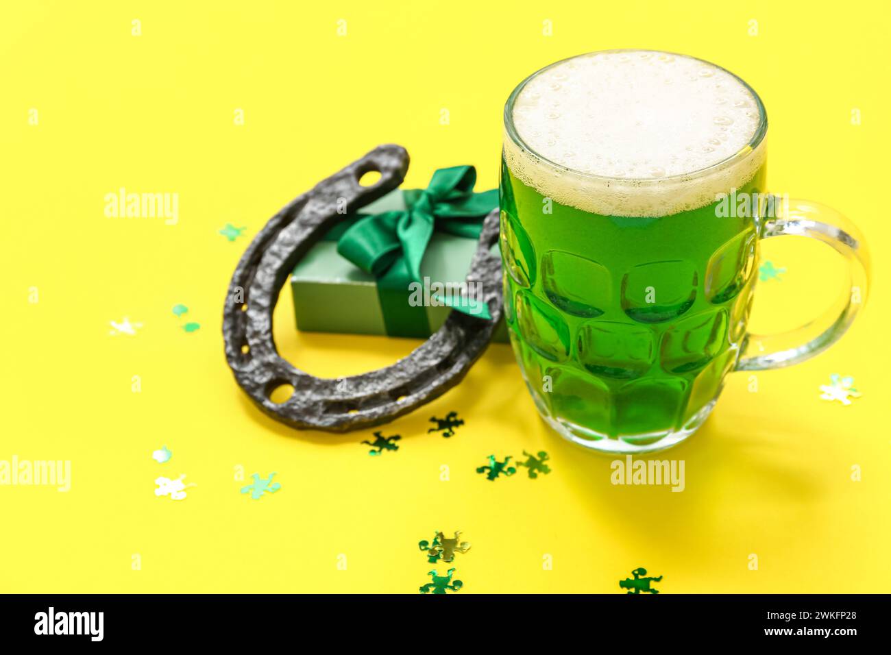 Bicchiere di birra con confezione regalo e ferro di cavallo su sfondo giallo. St Festa di Patrick Foto Stock