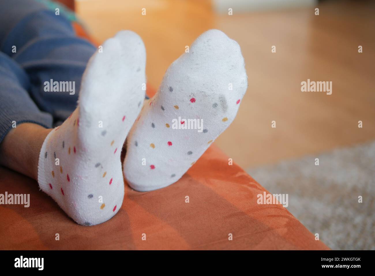 una persona si sta sdraiando su un divano con i piedi in alto e indossa calze a pois bianche Foto Stock