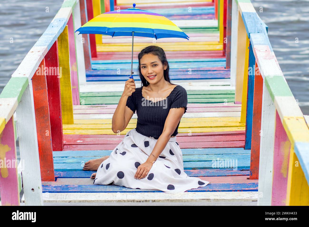 Una giovane donna con un ombrellone siede su una passerella colorata sopra il mare Foto Stock