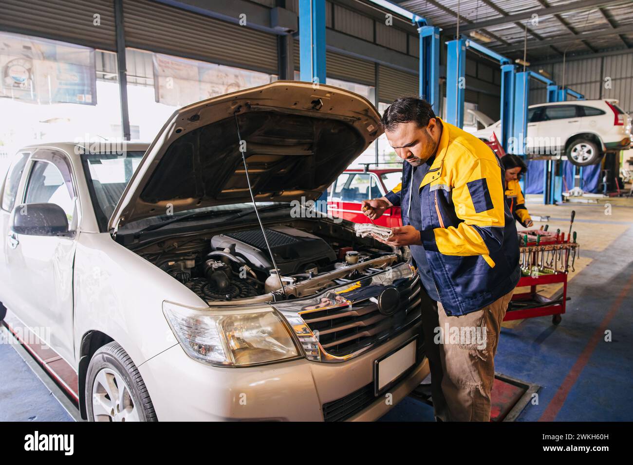 Lavoratore meccanico auto garage controllo livello olio motore bastone nel centro di assistenza auto, indiano professionale lavoro maschile Foto Stock