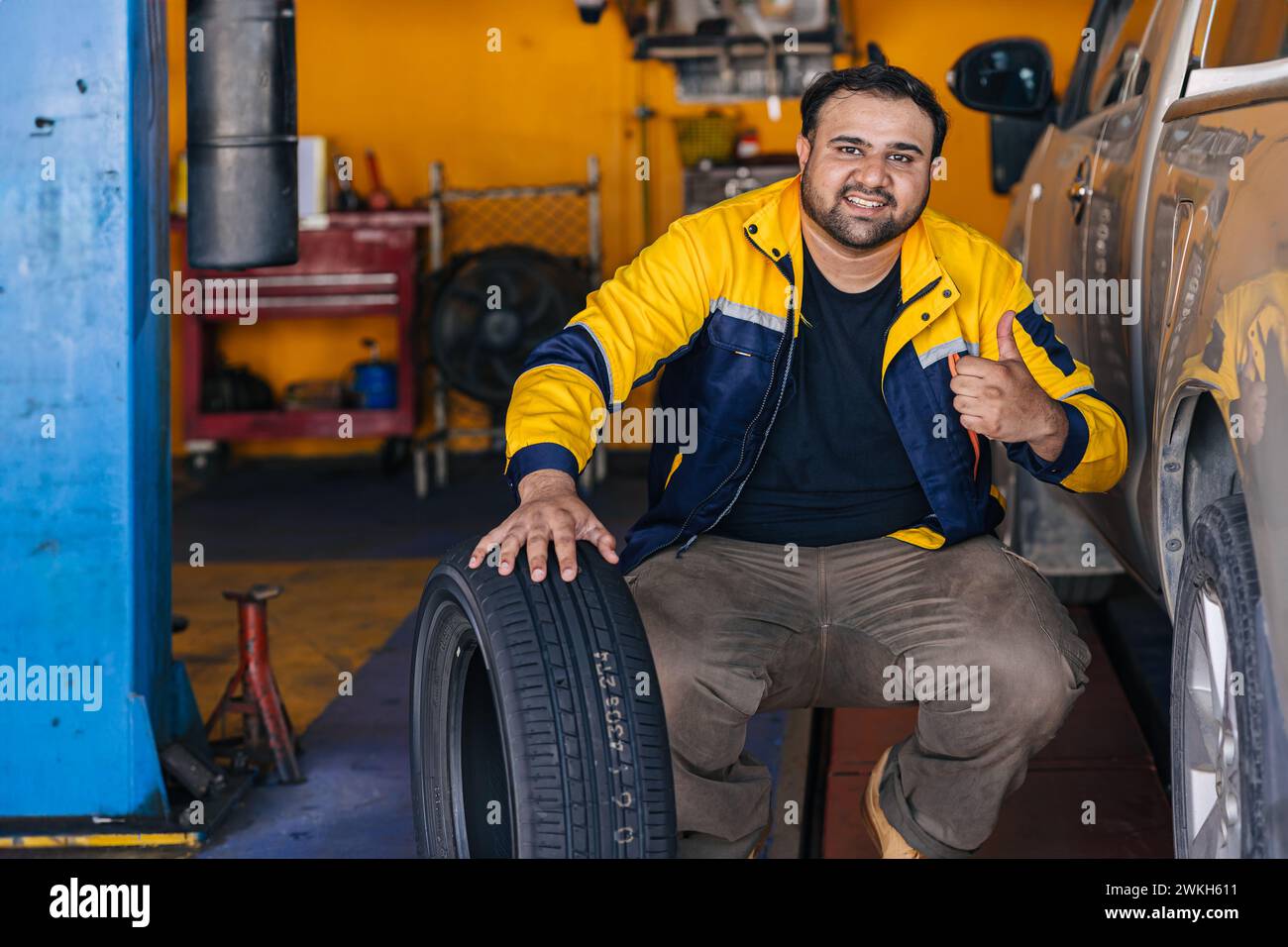 Ritratto indiano uomo lavoratore in garage auto meccanico felice lavoro servizio auto sostituire manutenzione veicolo pneumatico Foto Stock