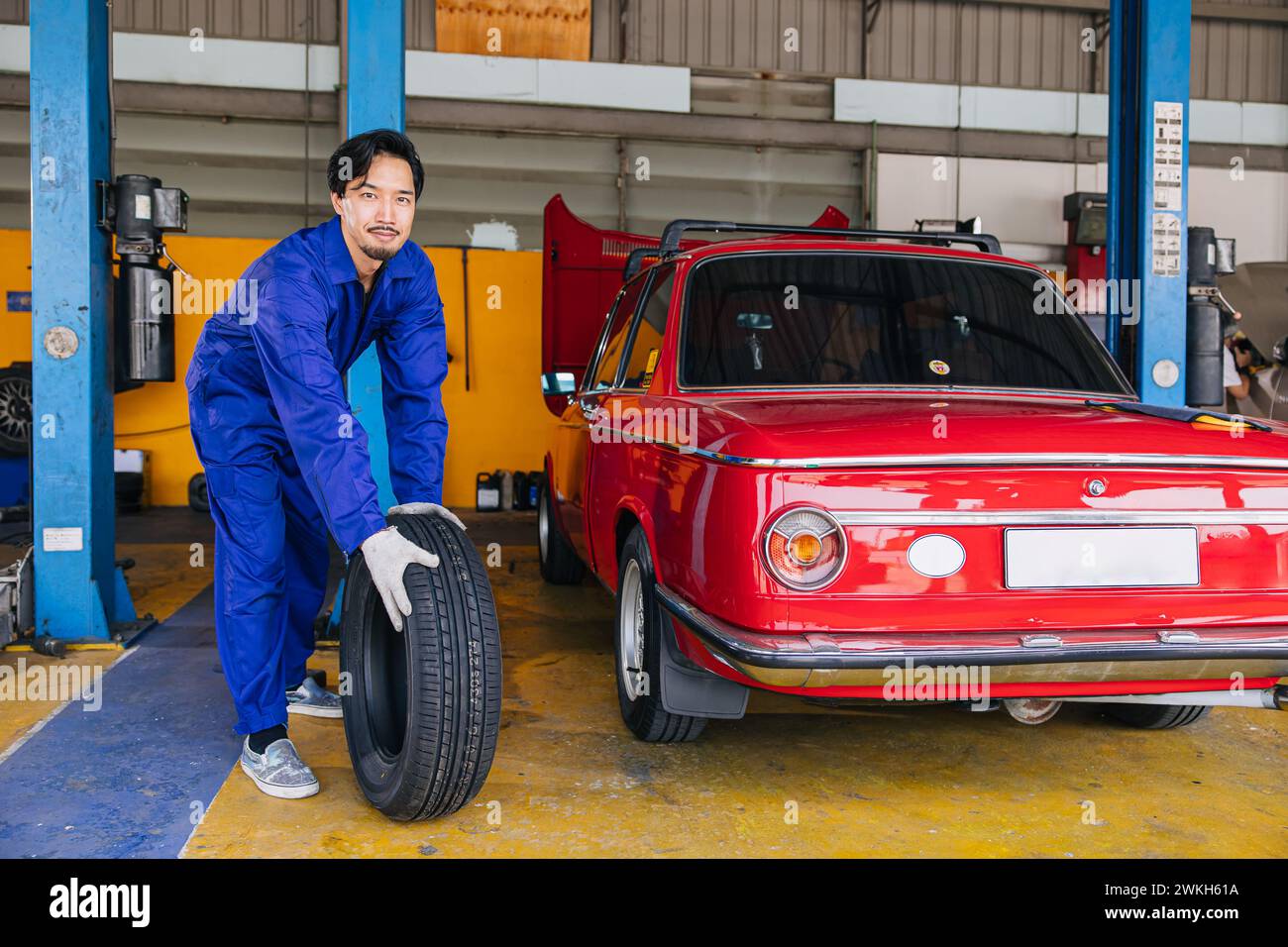 Asiatico giapponese maschio meccanico lavoratore ritratto in auto servizio officina auto pneumatico centro di manutenzione sostituire riparare parte auto Foto Stock