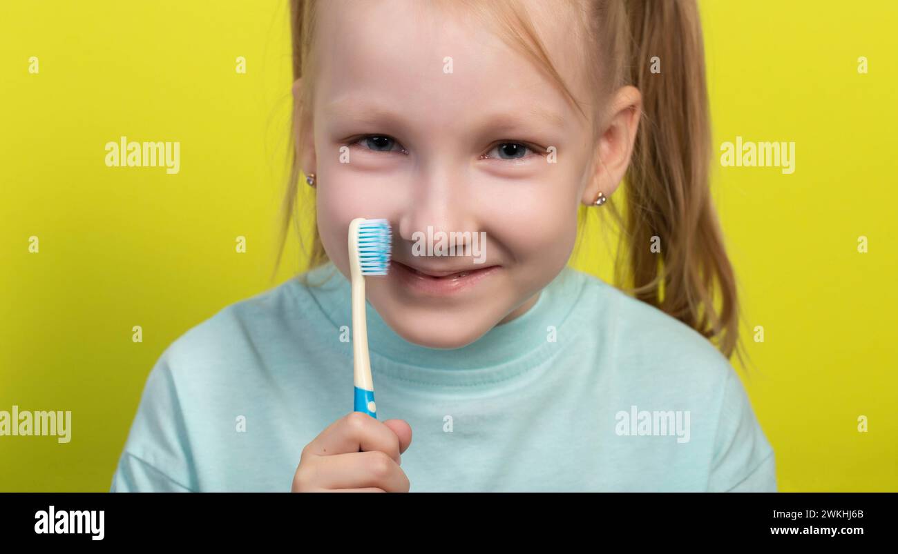 Ragazza sorridente di sette anni con uno spazzolino blu su sfondo giallo. Concetto di igiene orale e dentale. Pulizia dei denti per bambini, odontoiatria. Foto Stock