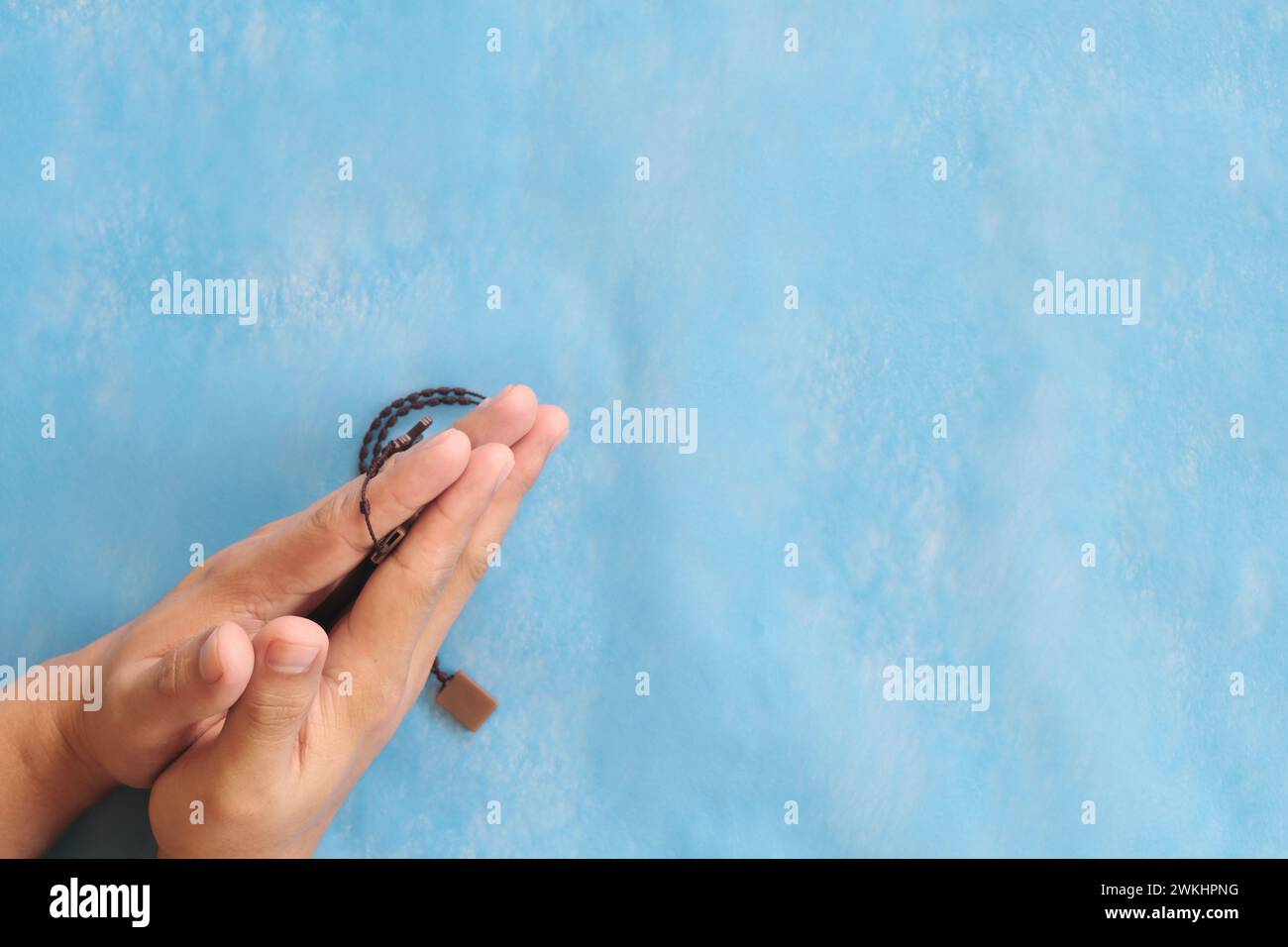 Le mani maschili si agganciarono, tenendo e pregando il rosario o lo scapolare su sfondo blu cielo. Foto Stock
